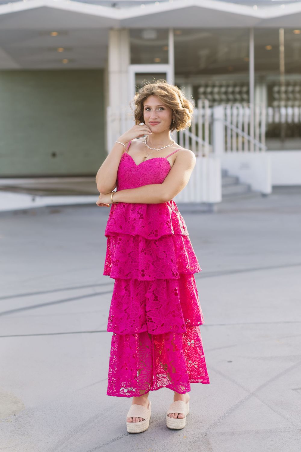 Someone wearing a vibrant hot pink tiered lace maxi dress and platform sandals poses outdoors.