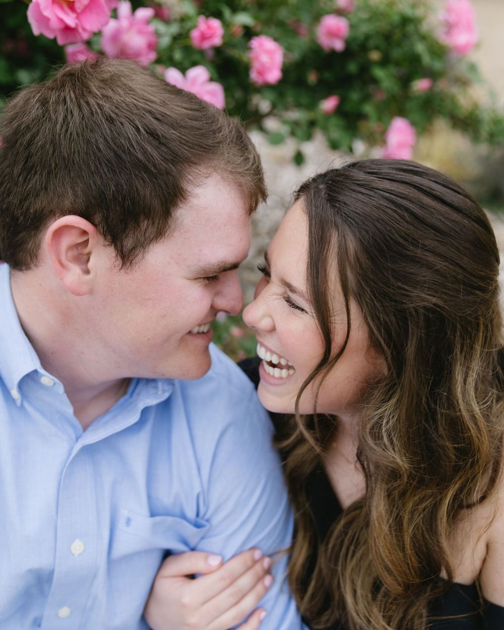 A romantic couple sharing a tender moment outdoors with pink flowers blooming in the background.