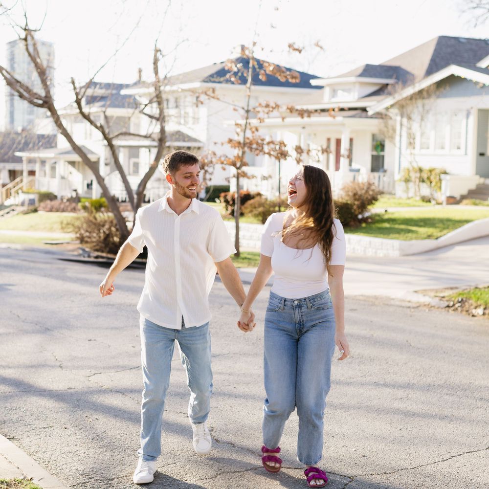 A couple holding hands while walking down a residential street on a sunny day.