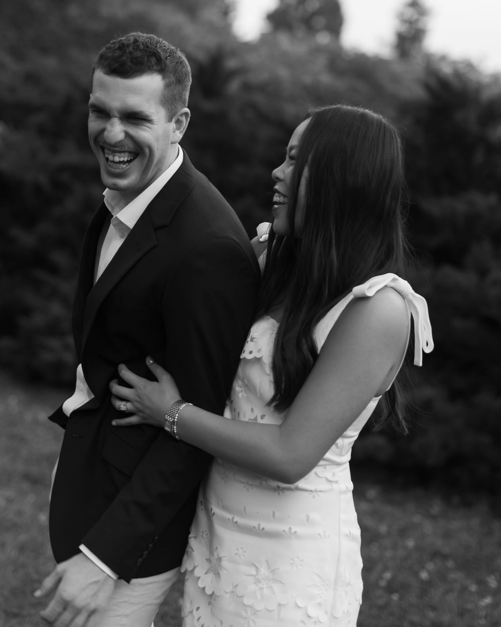 A black and white photo captures a candid laughing moment between newlyweds in formal attire.