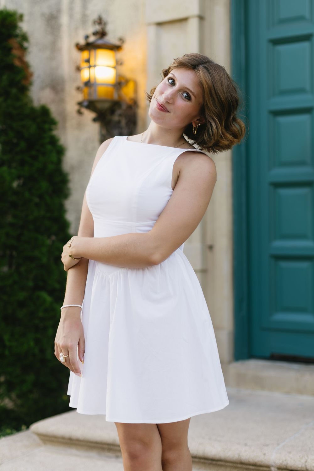 A white sleeveless summer dress is shown against a backdrop with a turquoise door and glowing lantern.