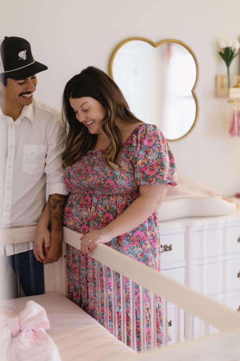 Expecting couple standing by baby crib in nursery with floral wallpaper.
