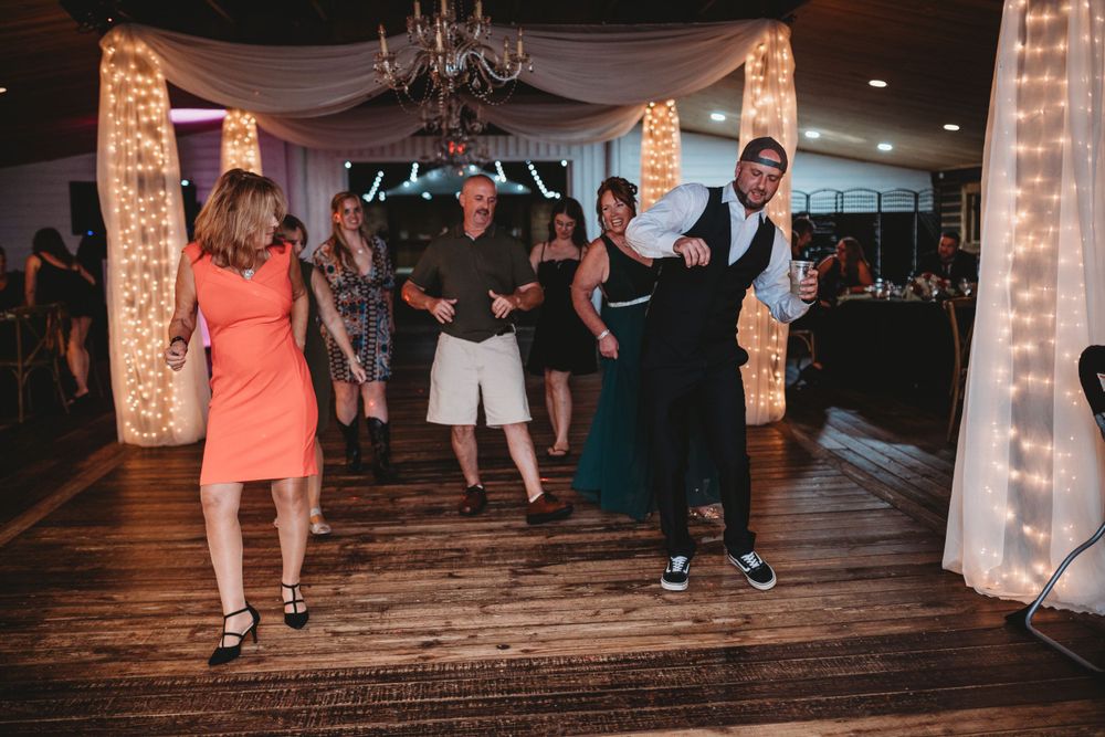 Wedding guests dancing on a wooden dance floor under white fabric draping and string lights.