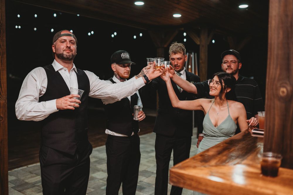 Groomsmen and wedding party members enjoying drinks and toasting at a wooden table.