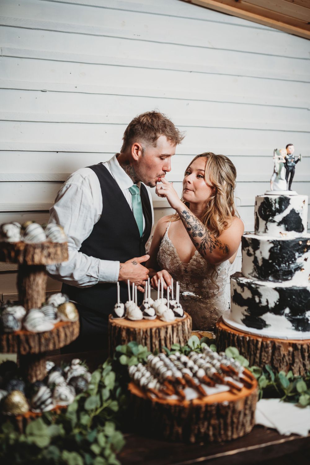 A couple share an intimate moment at their wedding dessert table featuring rustic wood slice cake stands.