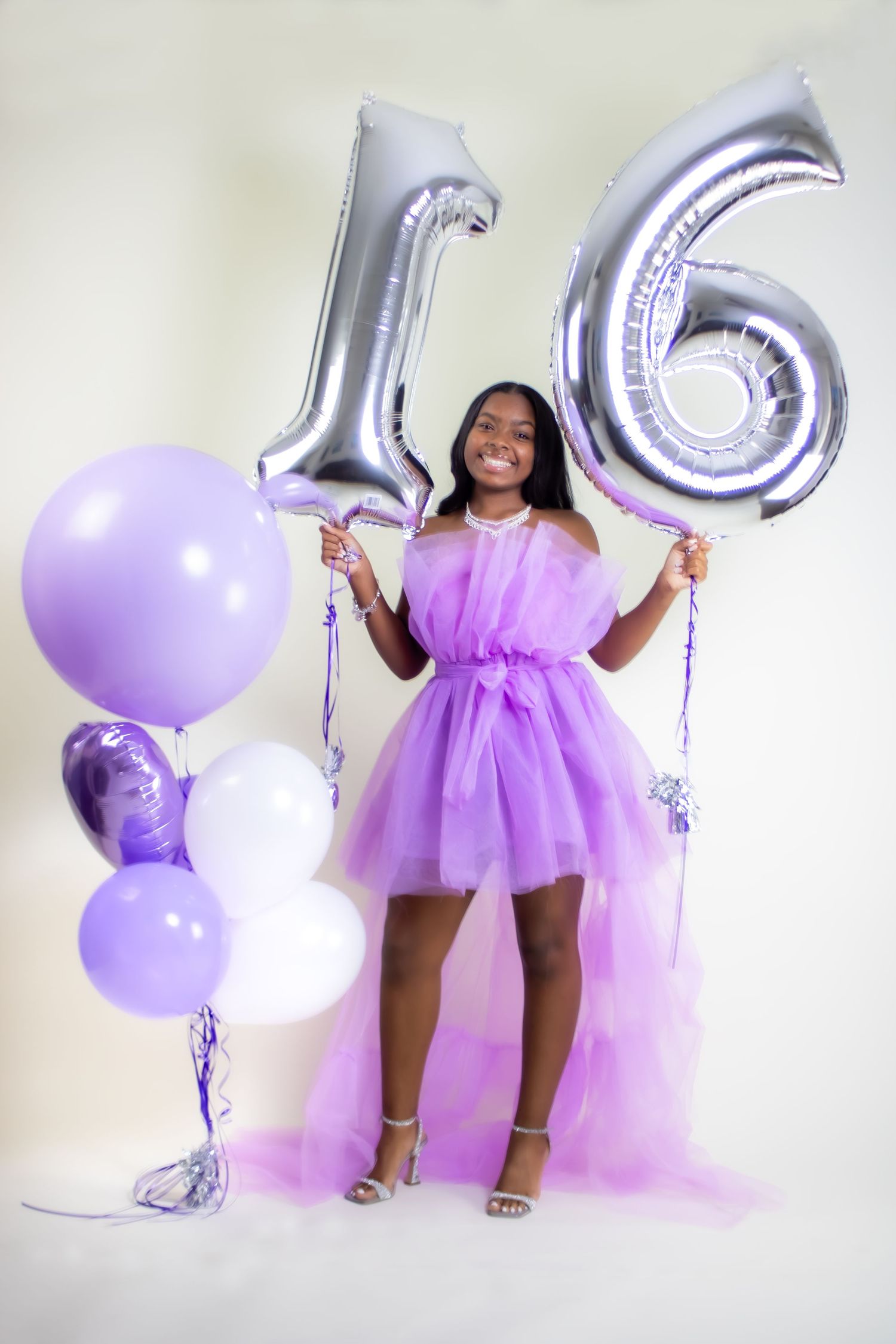 Sweet sixteen celebration with purple tulle dress and silver number balloons.