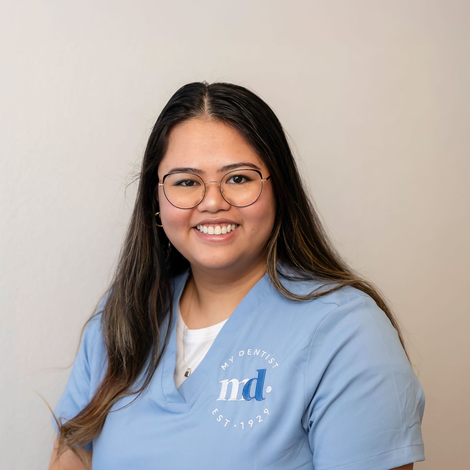 A person wearing glasses and a light blue sweatshirt smiles warmly at the camera in a professional headshot.