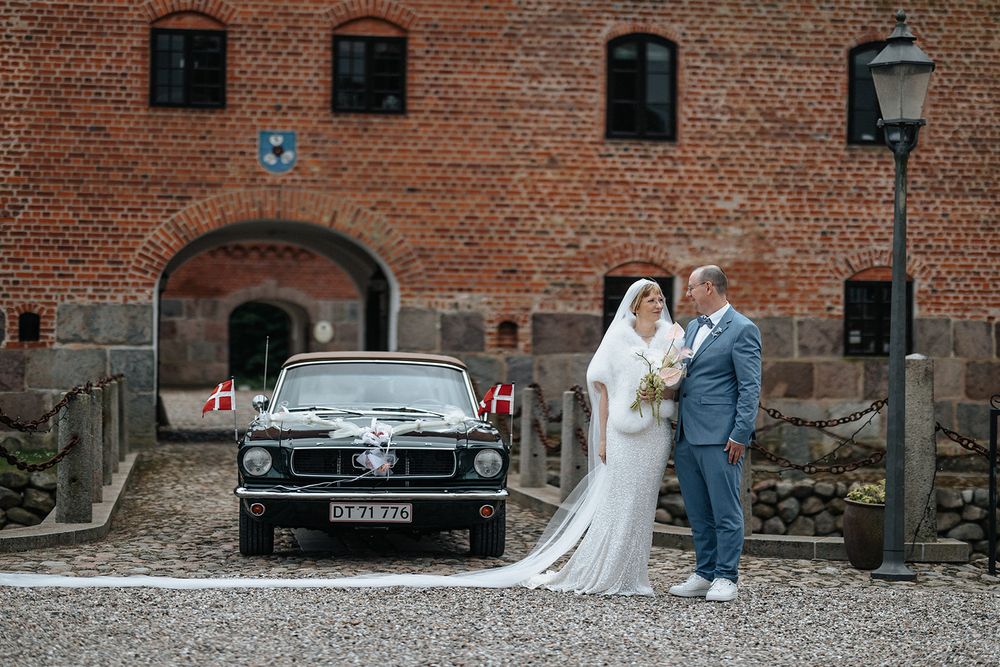 A classic black vintage car parked in front of a rustic brick building during a wedding photoshoot.