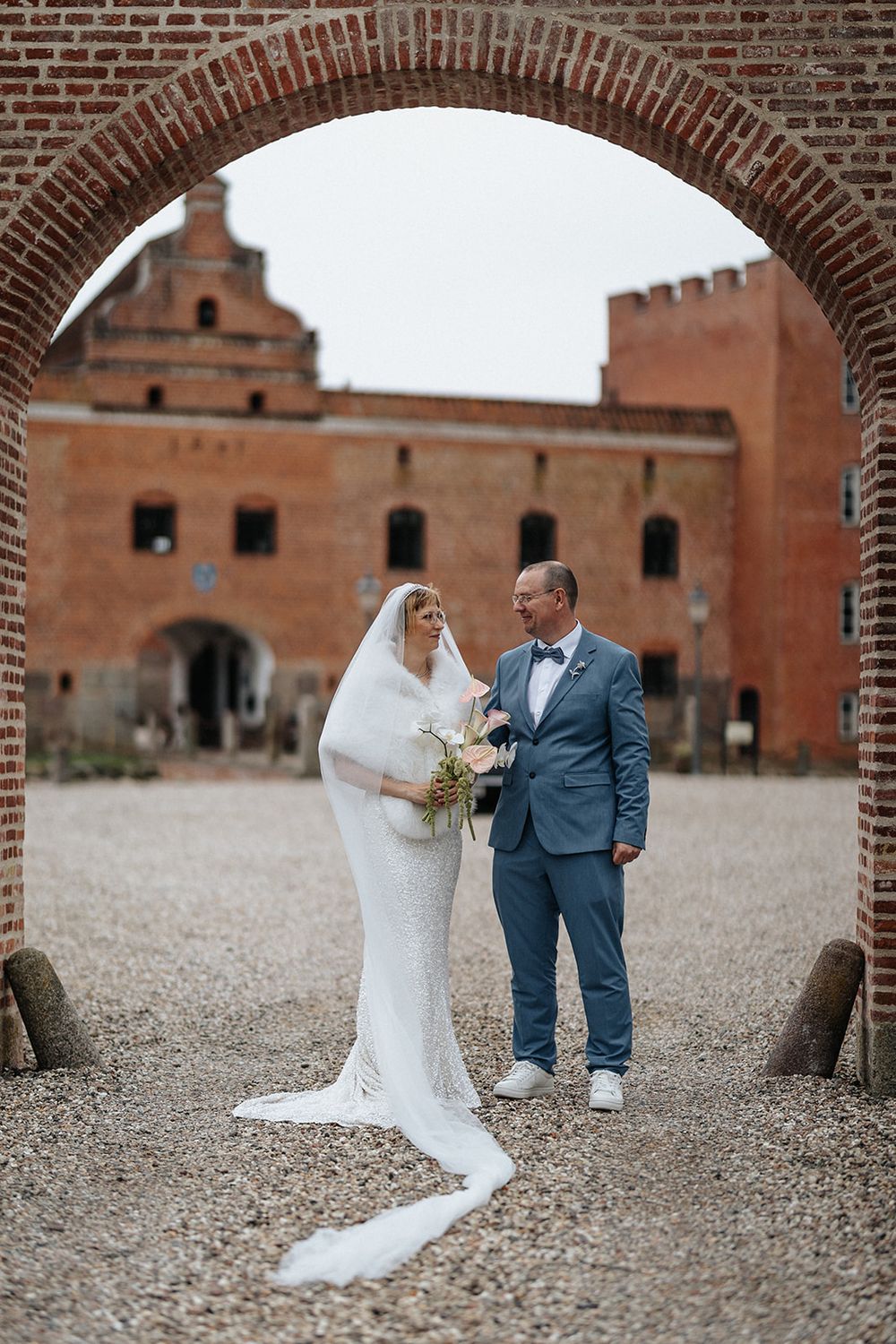 A romantic wedding moment captured through brick archways at a rustic venue with cobblestone ground.