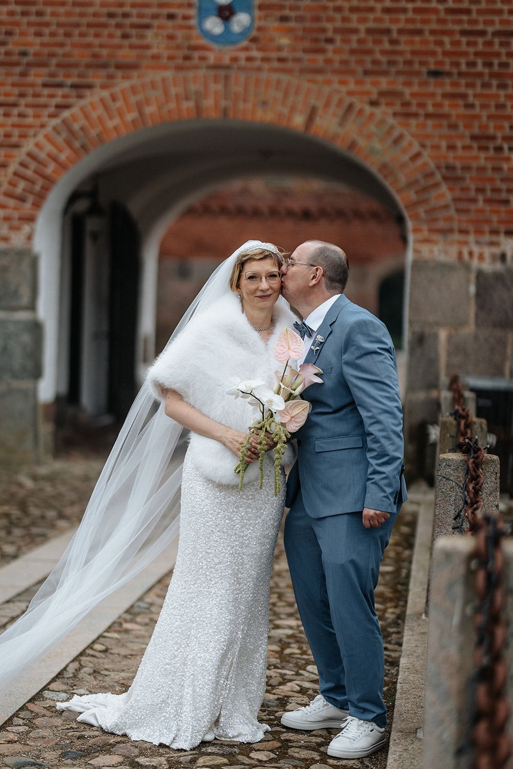 Newlywed couple shares romantic moments in front of rustic brick wall during wedding photoshoot.