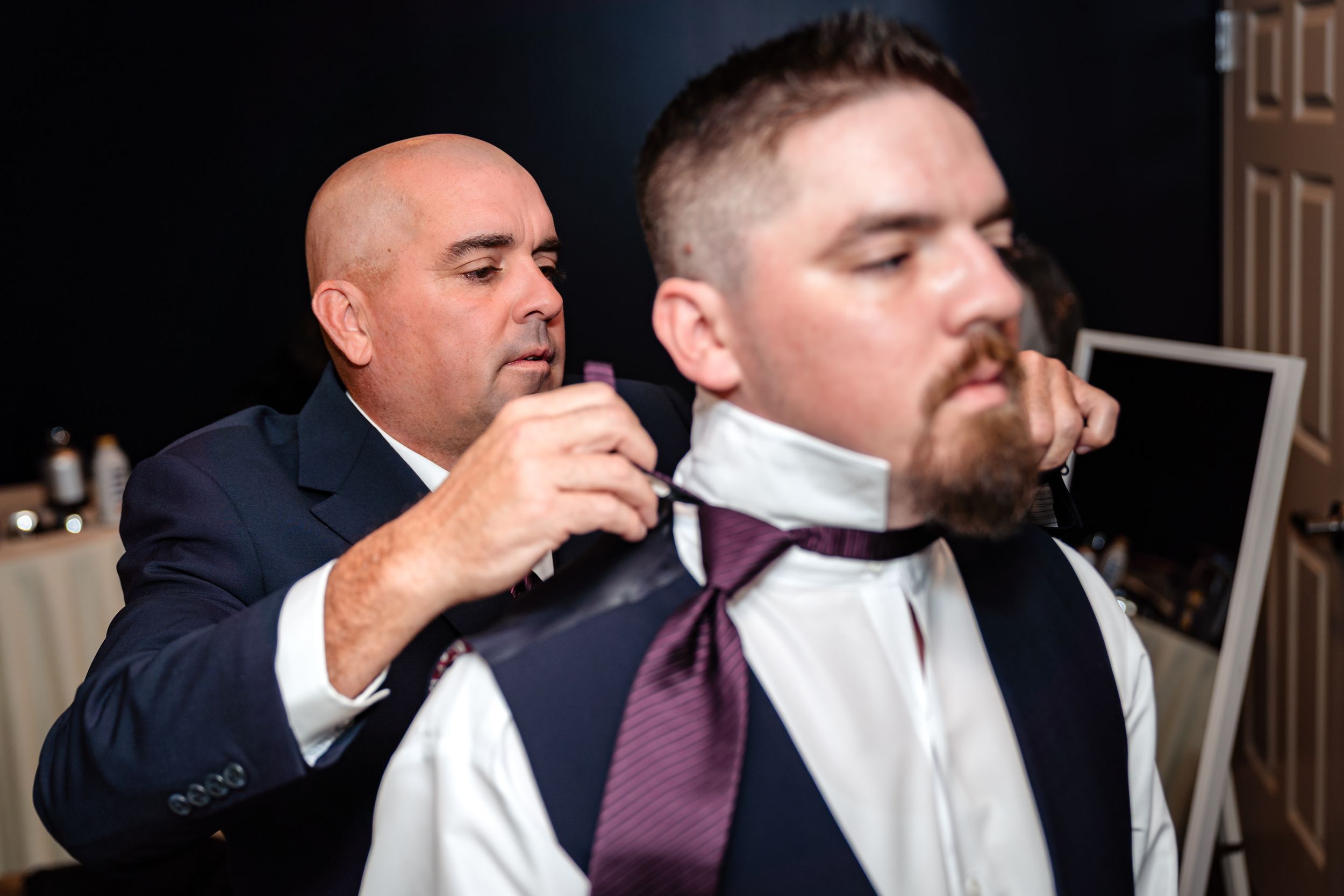 Wedding party members in navy suits and purple ties make final adjustments to their formal attire.