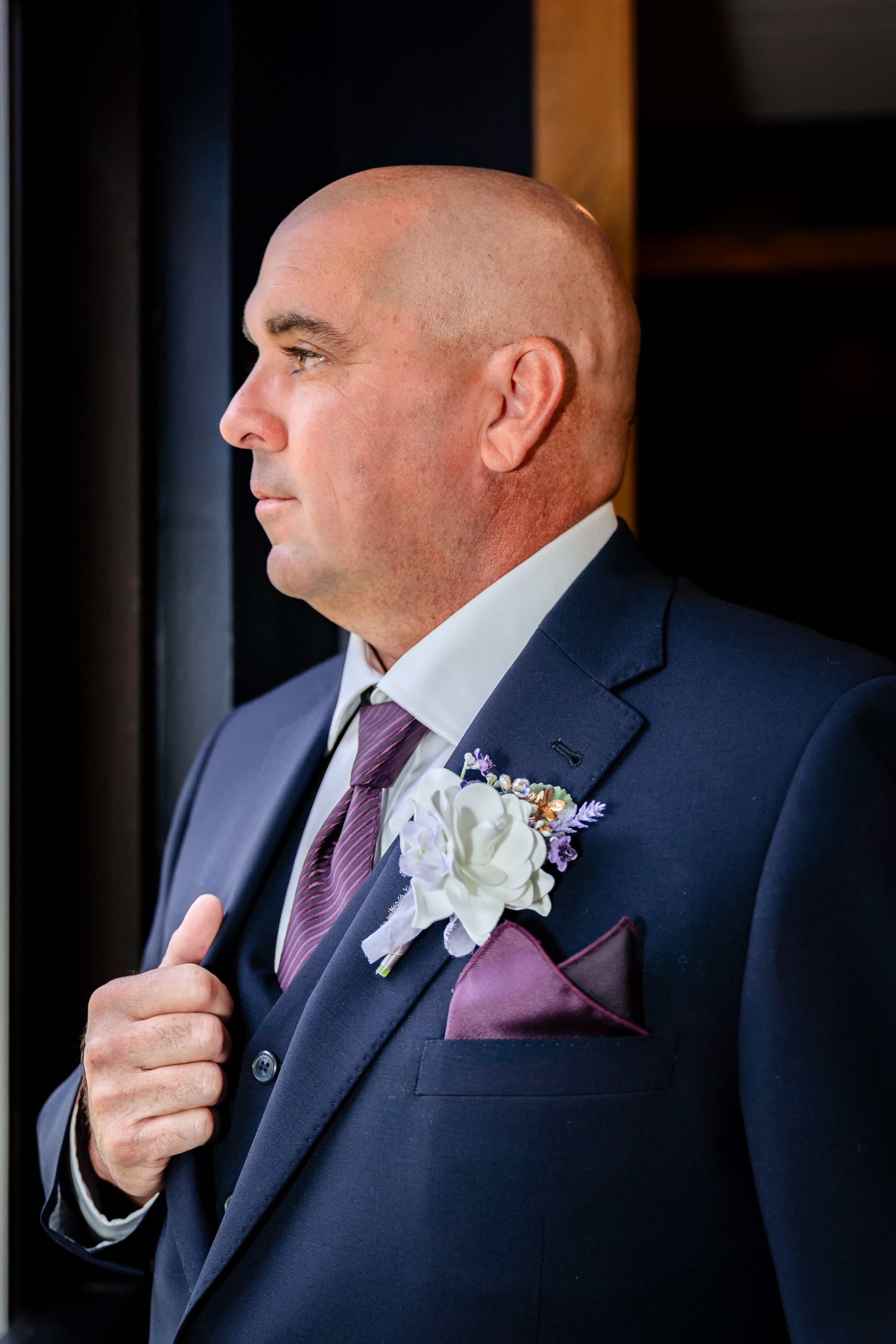 Groomsman in navy suit with purple tie and boutonniere makes final adjustments before the ceremony.