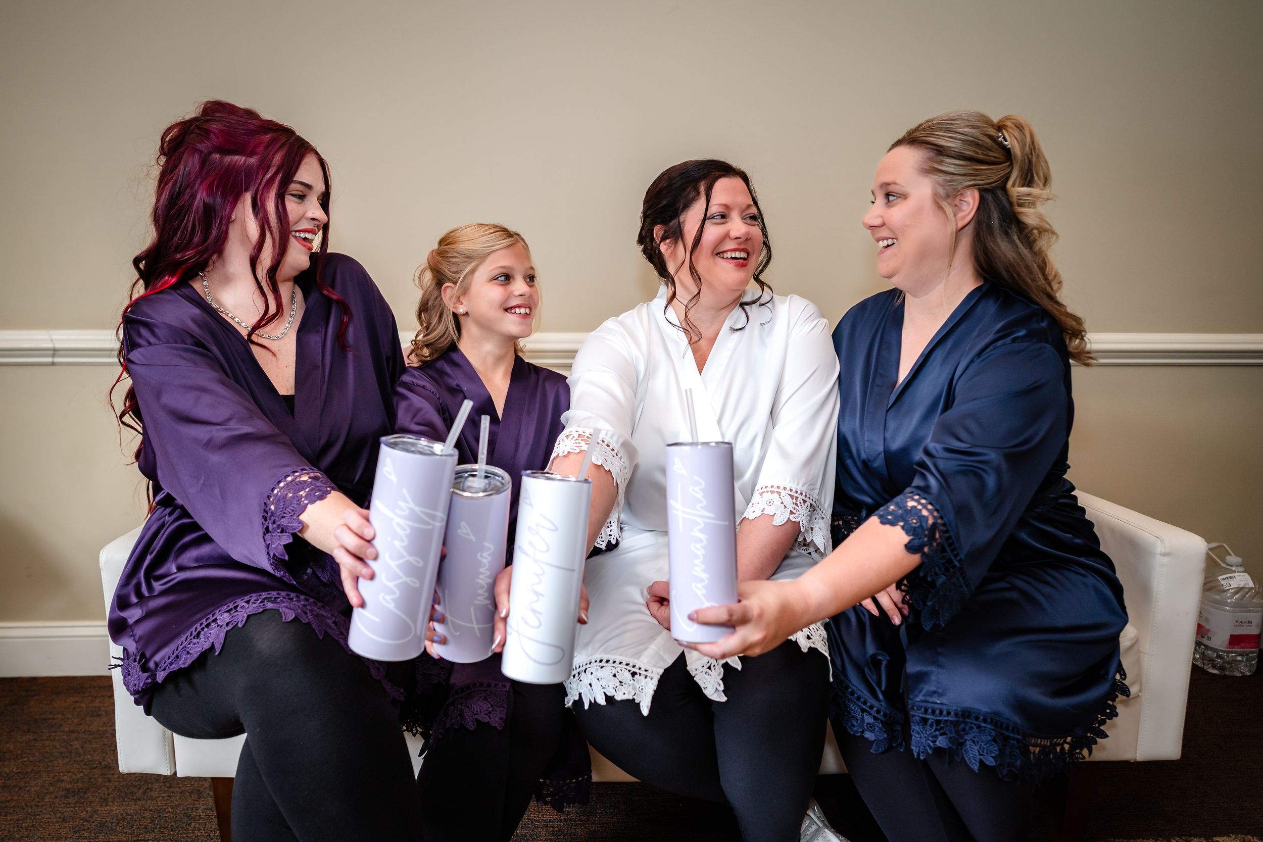 Bridesmaids in purple and navy robes share laughs while getting ready for the wedding.
