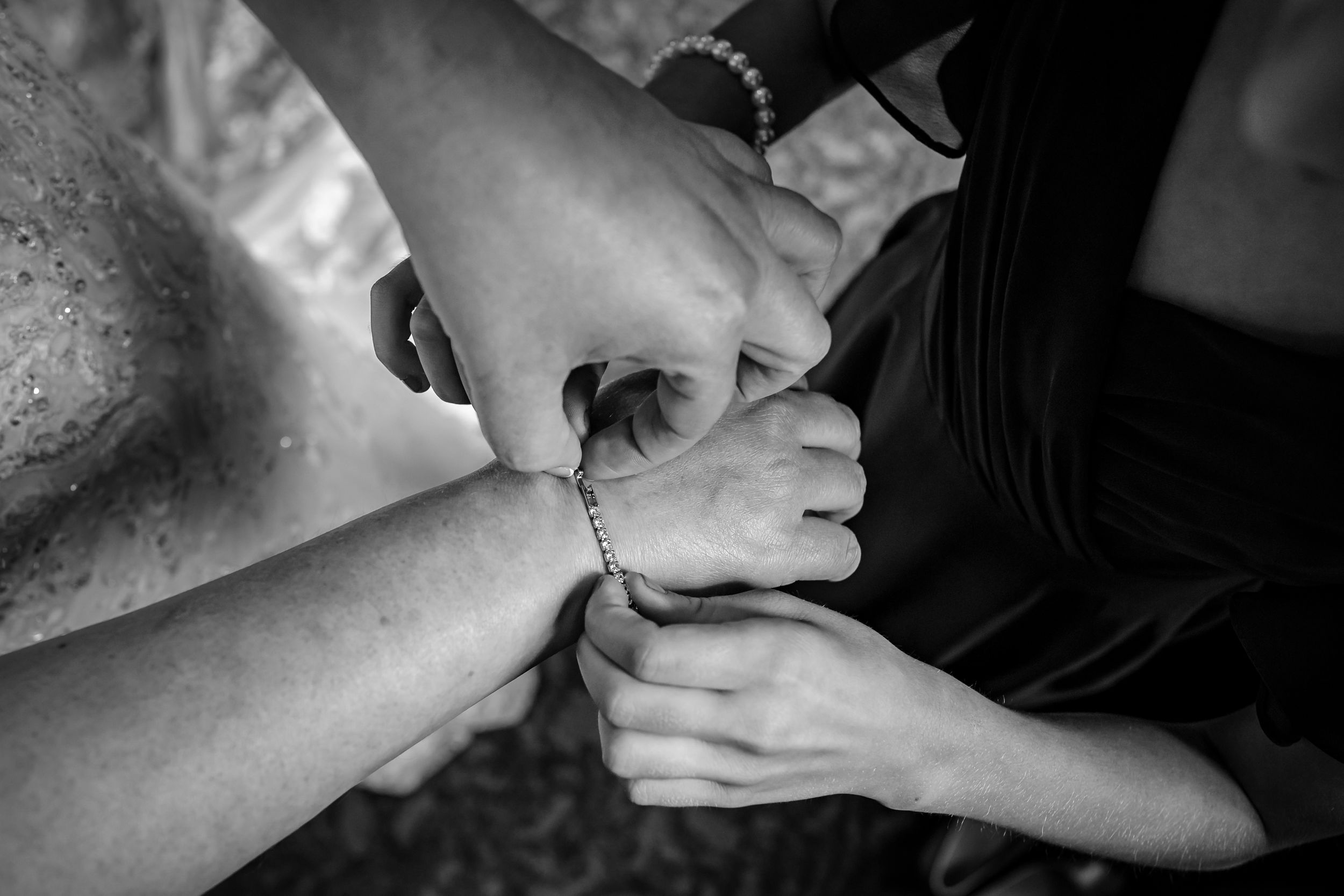 Close-up black and white shot of hands helping with wedding dress preparations.