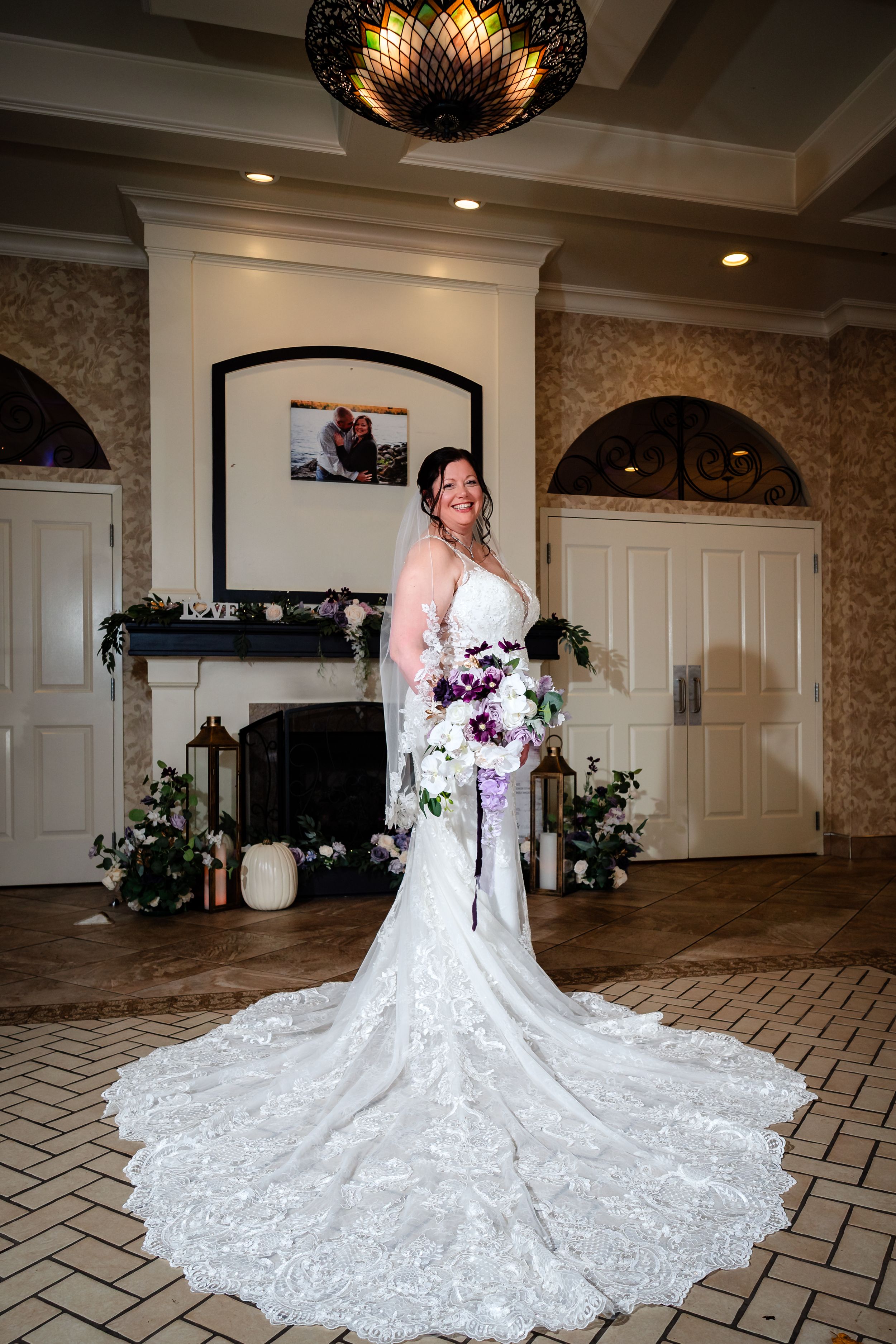 Stunning bride in lace wedding gown with long train poses in elegant venue with fireplace.