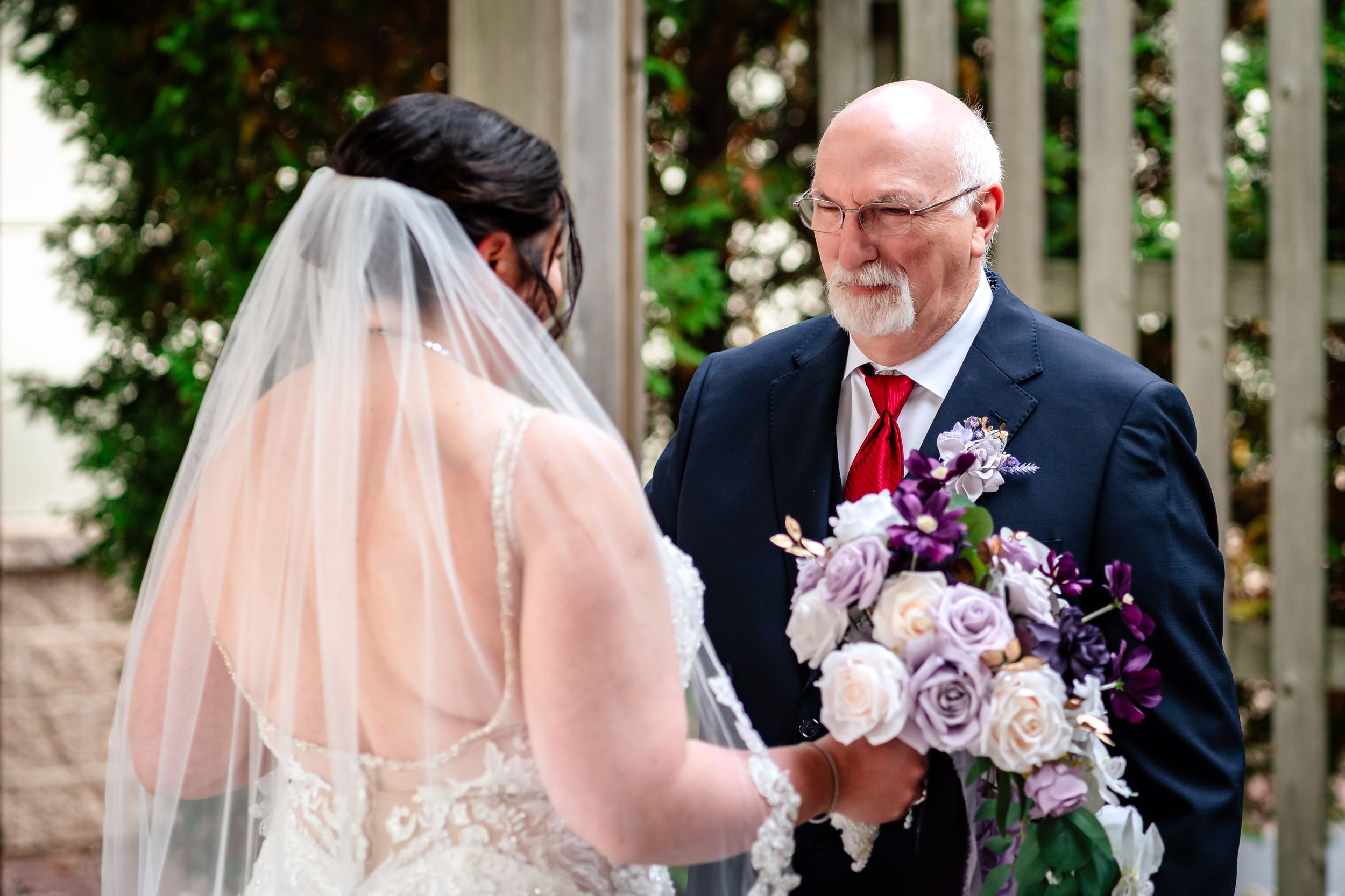 Wedding ceremony moment with purple and white floral bouquet in outdoor garden setting.