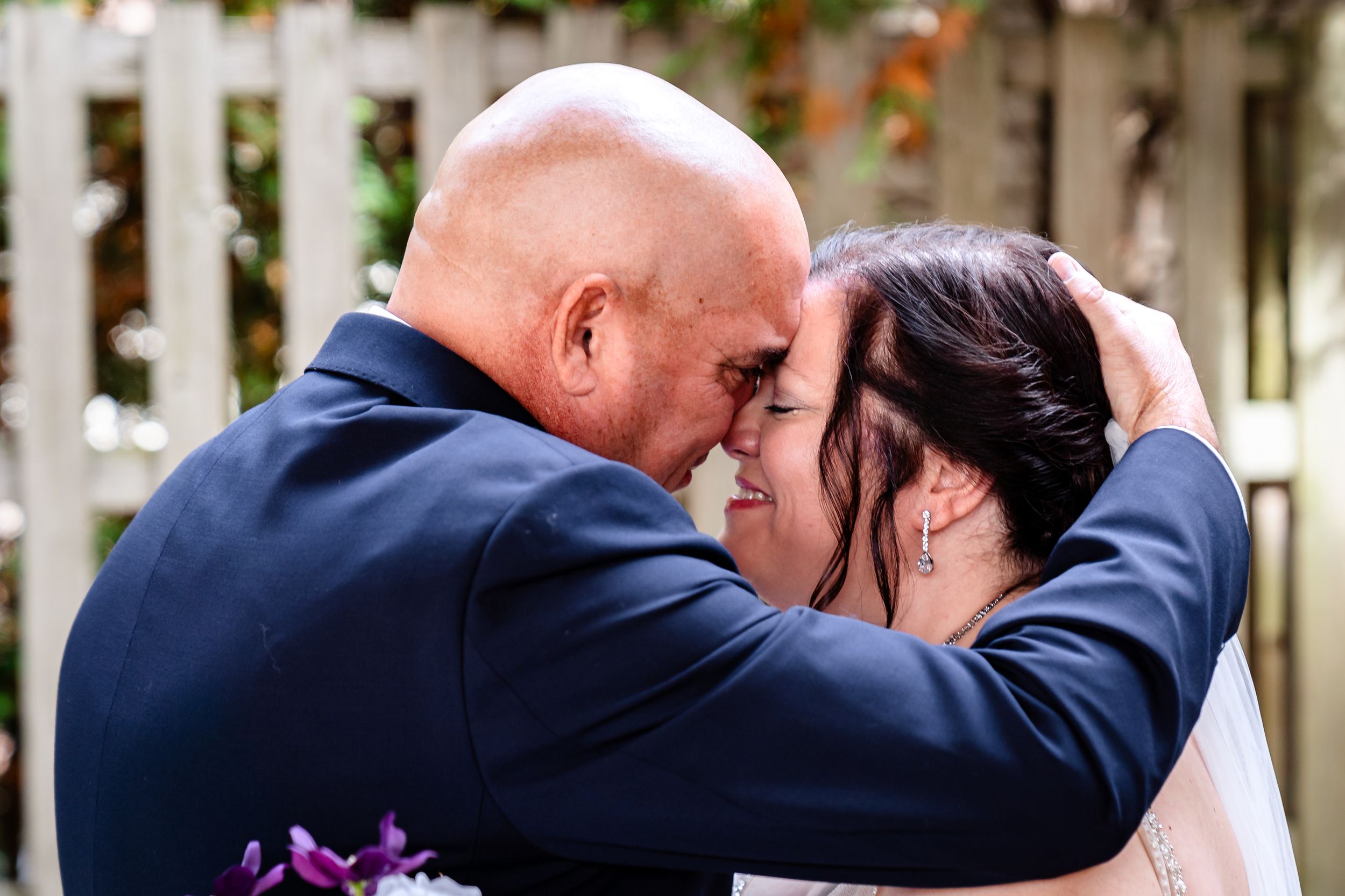 Tender wedding kiss photographed against white lattice garden backdrop.