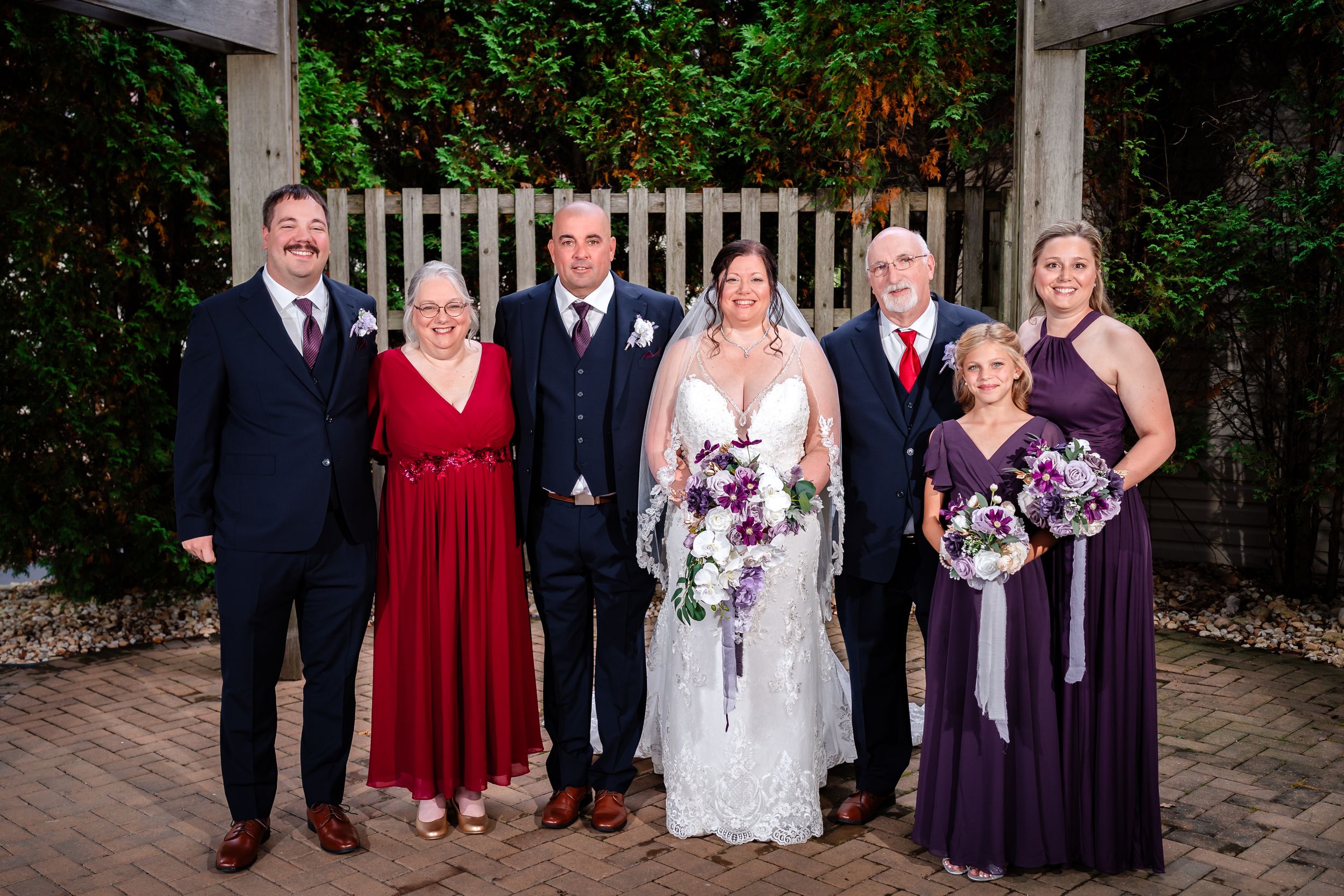 Wedding group photo with bridesmaids in purple dresses and groomsmen in dark suits.
