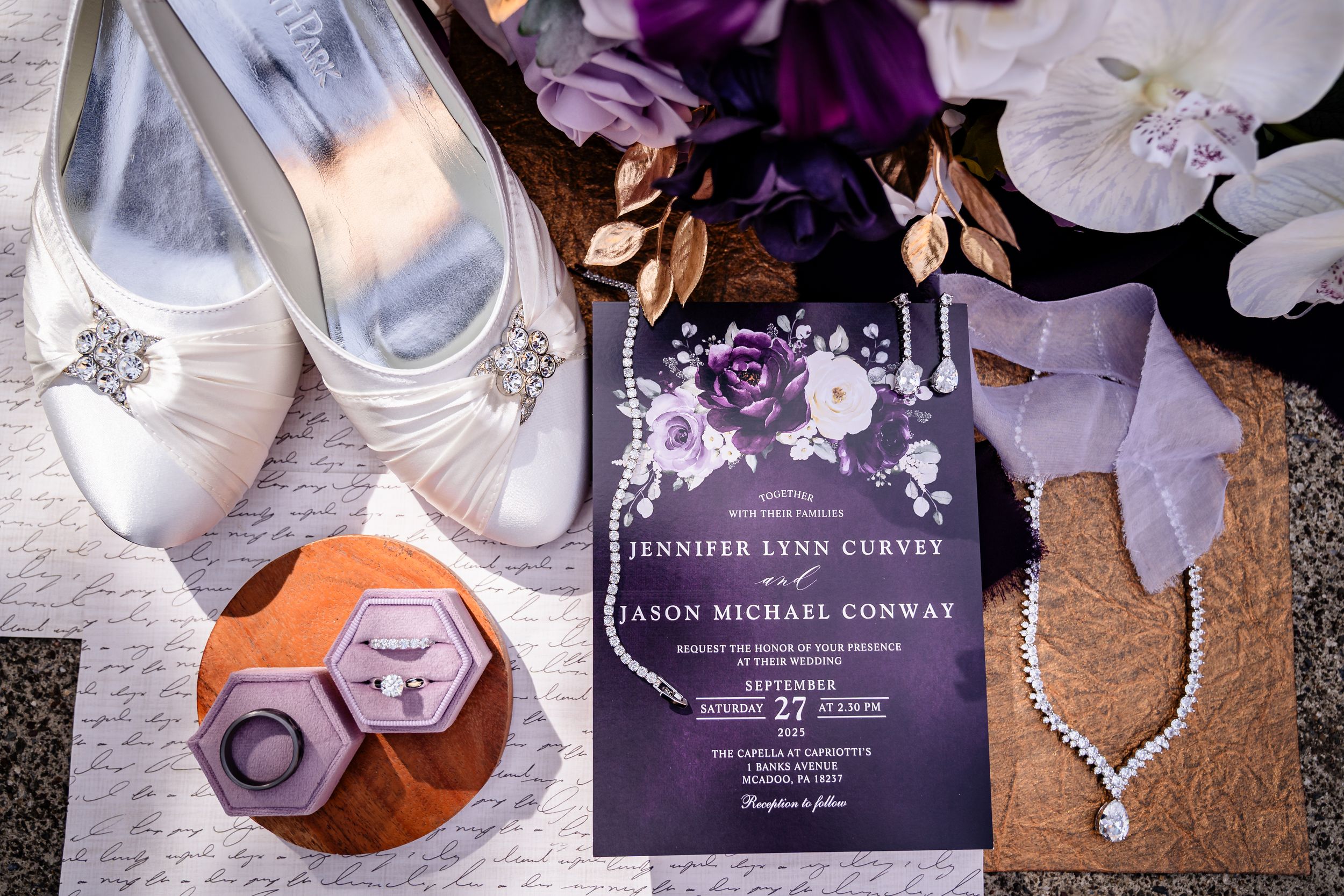 Wedding details including purple invitations, jewelry, and white bridal shoes arranged artistically.