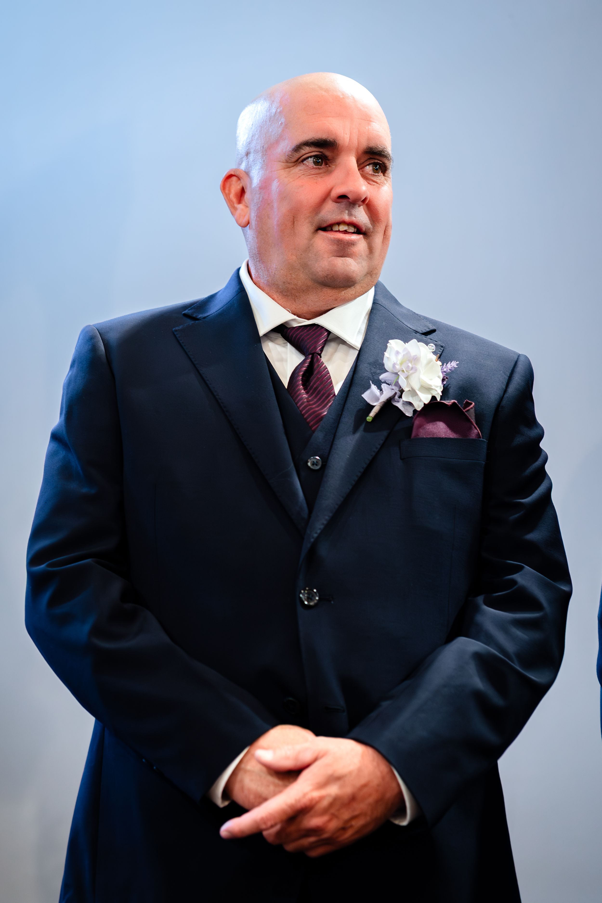 A man in a dark suit with a white boutonniere poses in a series of wedding photos.