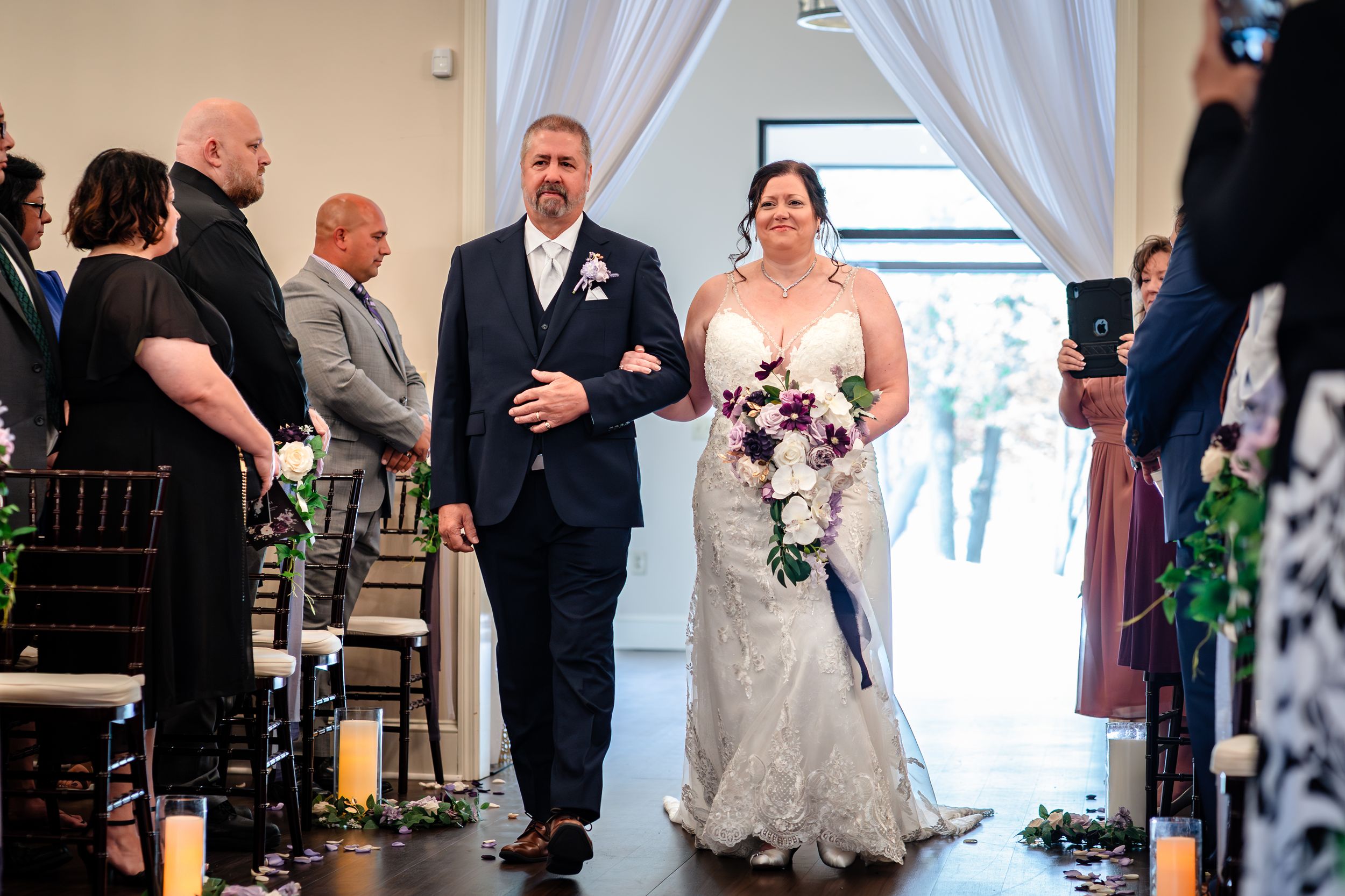 Wedding ceremony in an elegant indoor venue with white drapes and guests seated in rows.