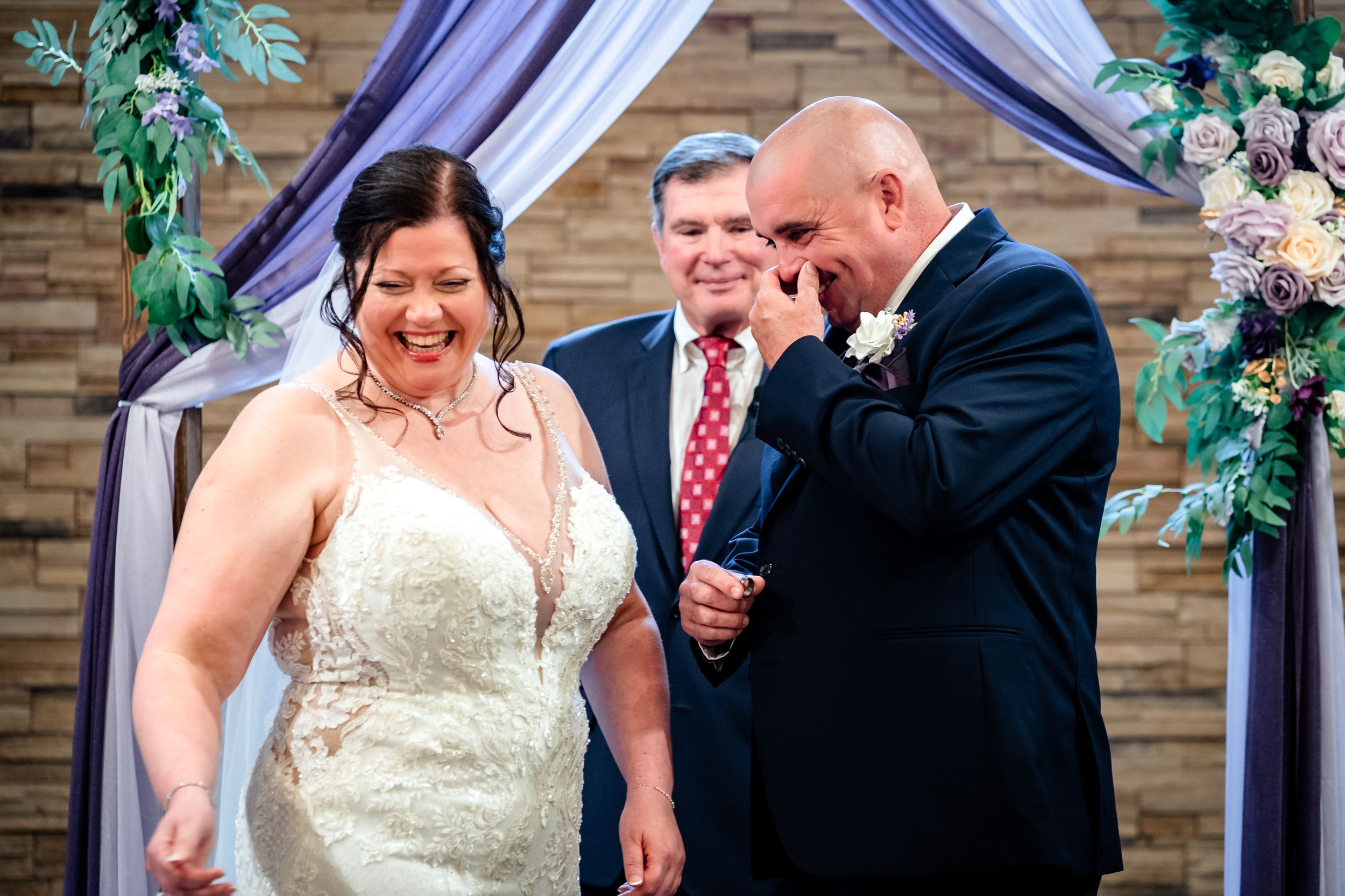 Wedding ceremony moment under purple draping with floral decorations.