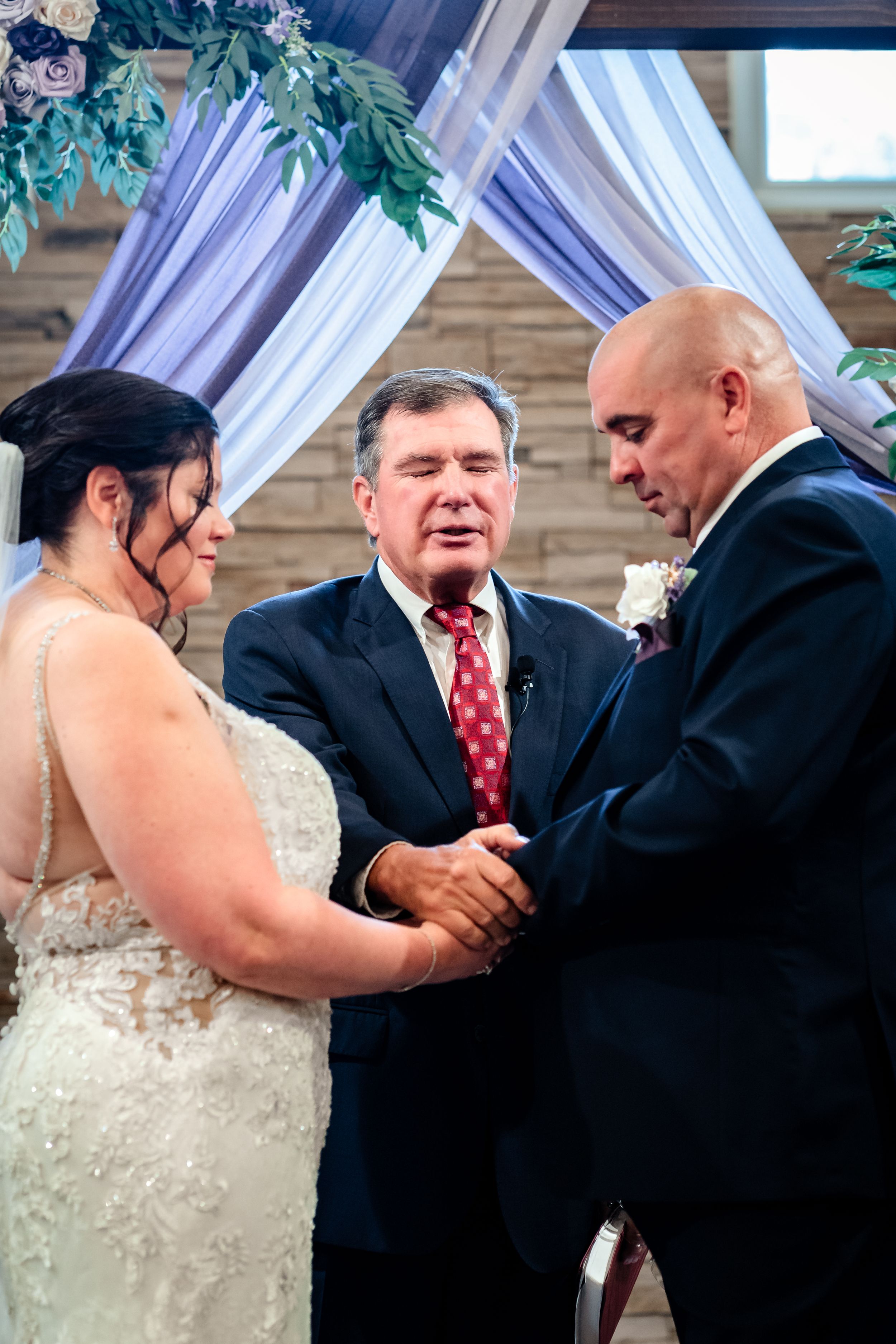 Intimate wedding ceremony moment under purple draped arch with greenery.