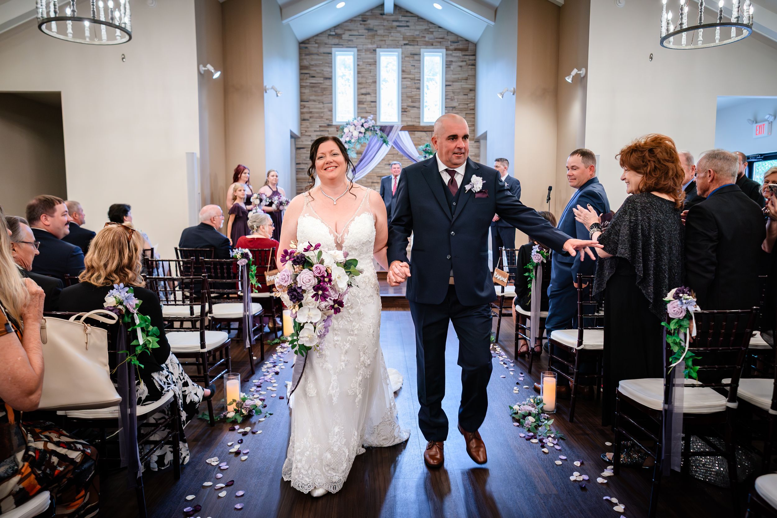 Wedding guests seated in rows at an indoor ceremony venue with stone accent walls.