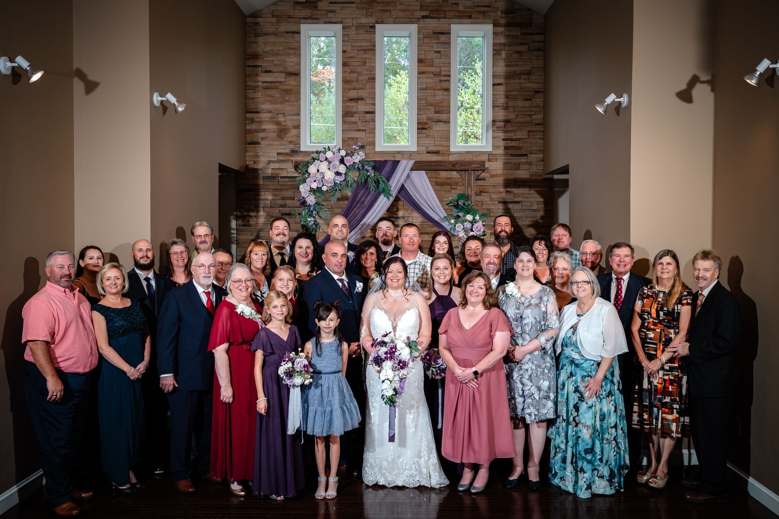 Large group wedding photo with guests gathered in formal attire inside a chapel.