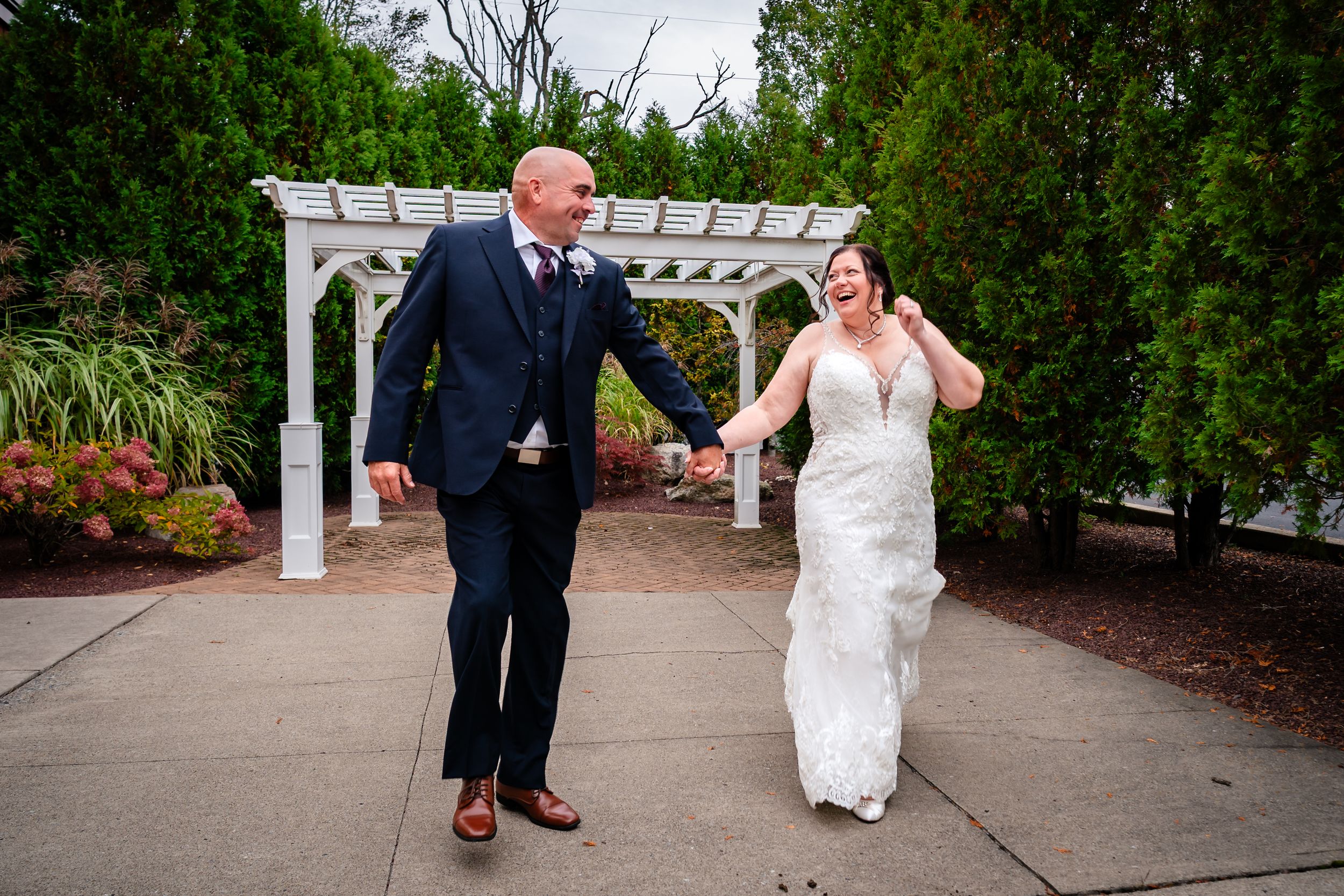 Outdoor wedding portraits taken in a garden setting with white pergola and greenery.