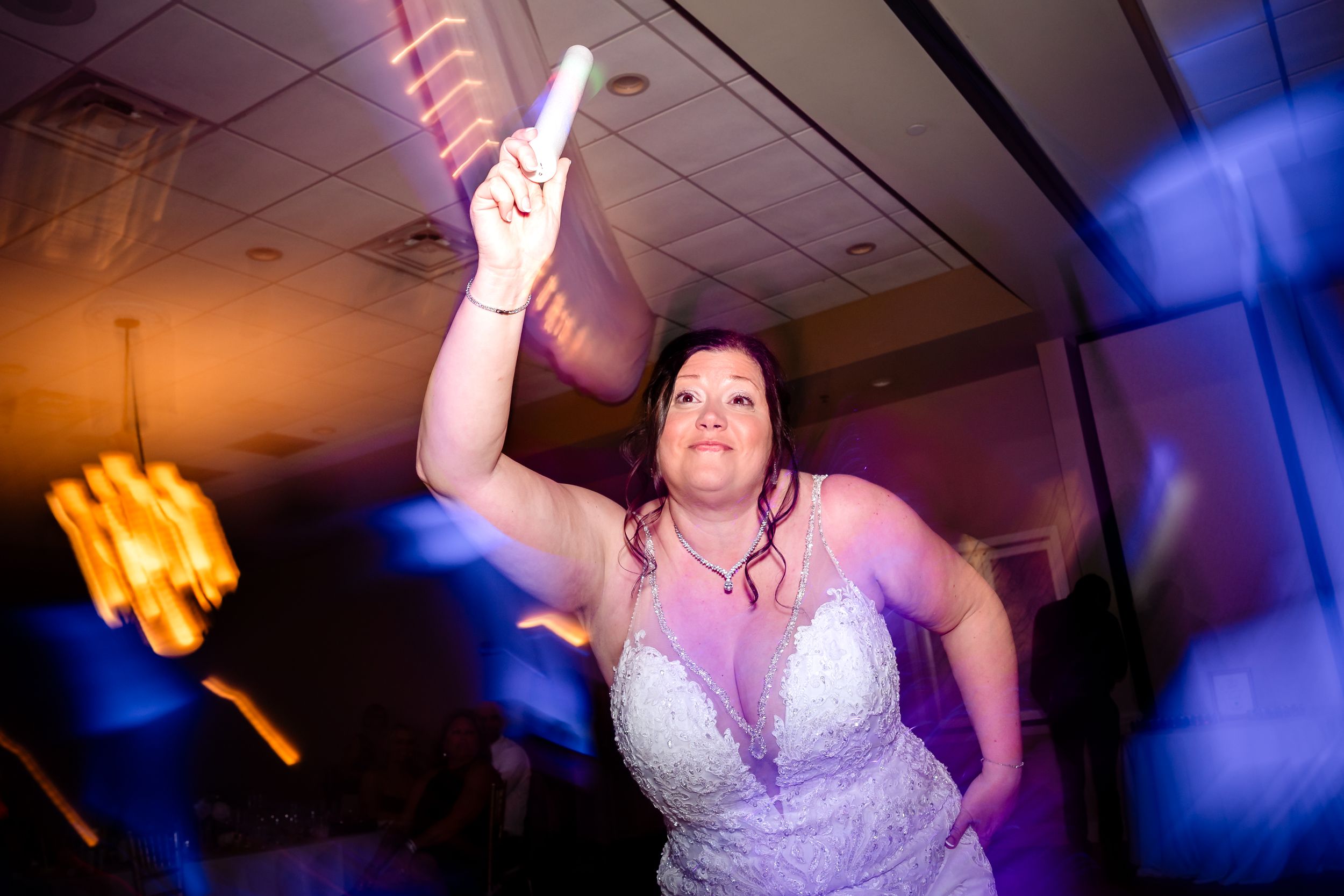 Bride dancing under dramatic purple and orange lighting at wedding reception.