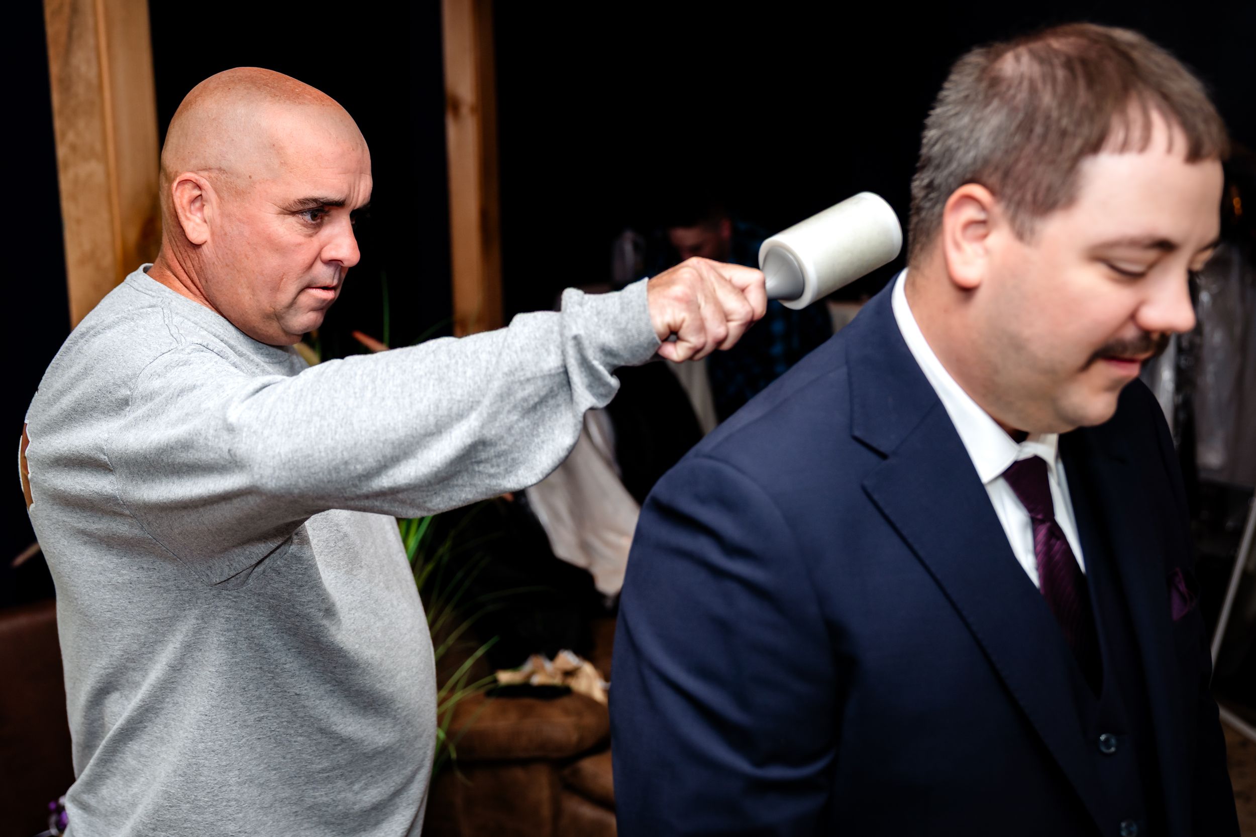 Groomsmen in navy suits help each other get ready by adjusting ties and boutonnieres before the wedding ceremony.