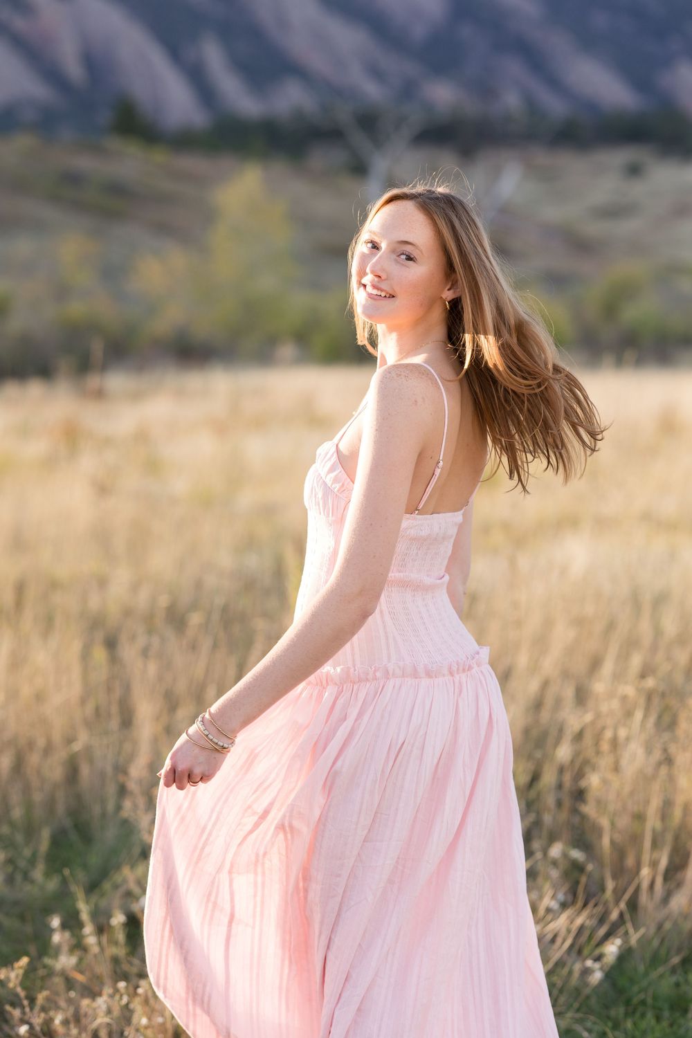 Flowing pink dress twirls gracefully in an outdoor setting with mountain scenery and tall grass.
