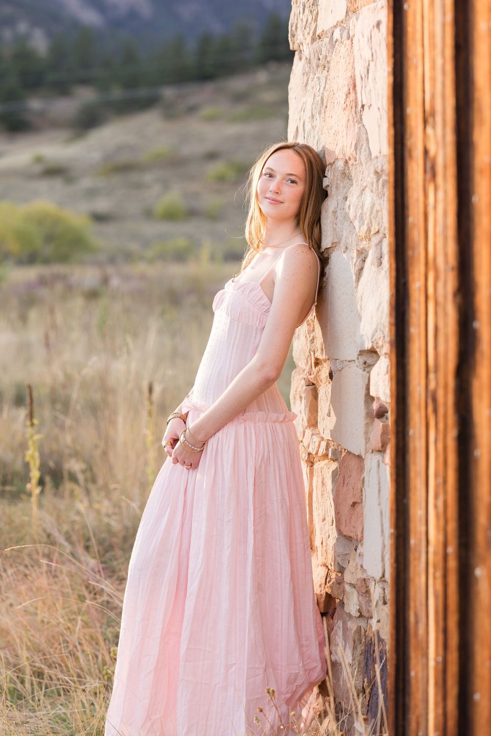 Rustic wooden post frames a dreamy scene with pink dress against natural mountain landscape.