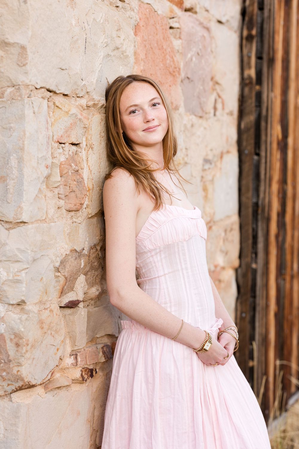 A soft pink dress stands out against weathered stone walls in an artistic portrait series.