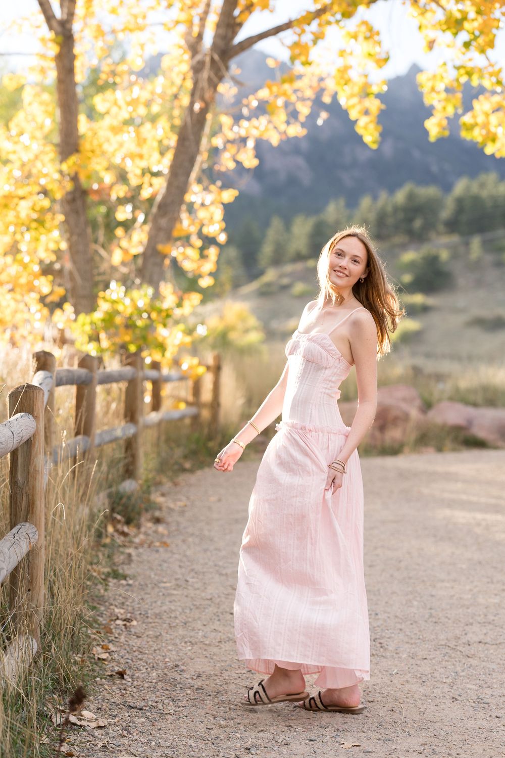 A person in a flowing pink dress twirls gracefully on a path surrounded by golden autumn trees.