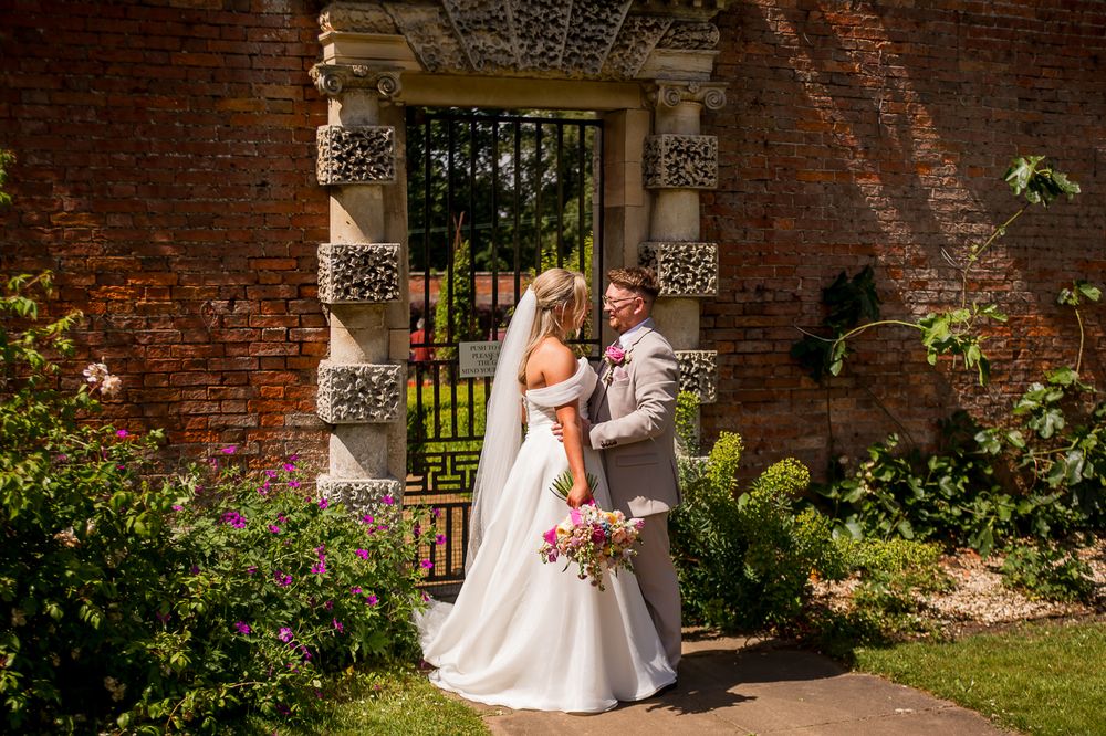 Romantic wedding photos taken under decorative stone archway in garden setting.