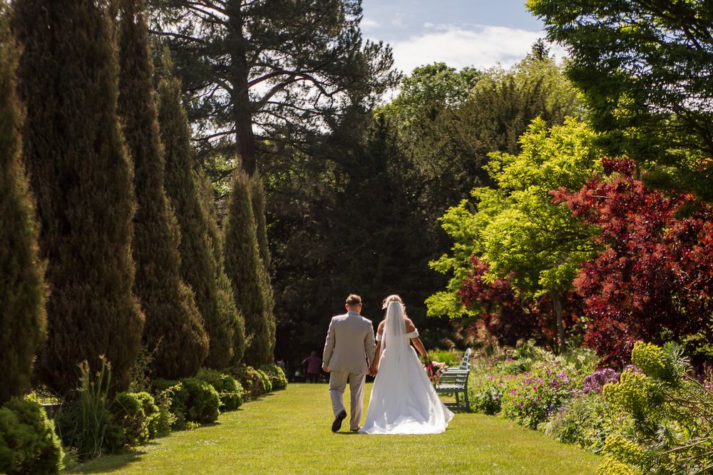 Couple strolls through scenic garden path with evergreen trees and flowering bushes.
