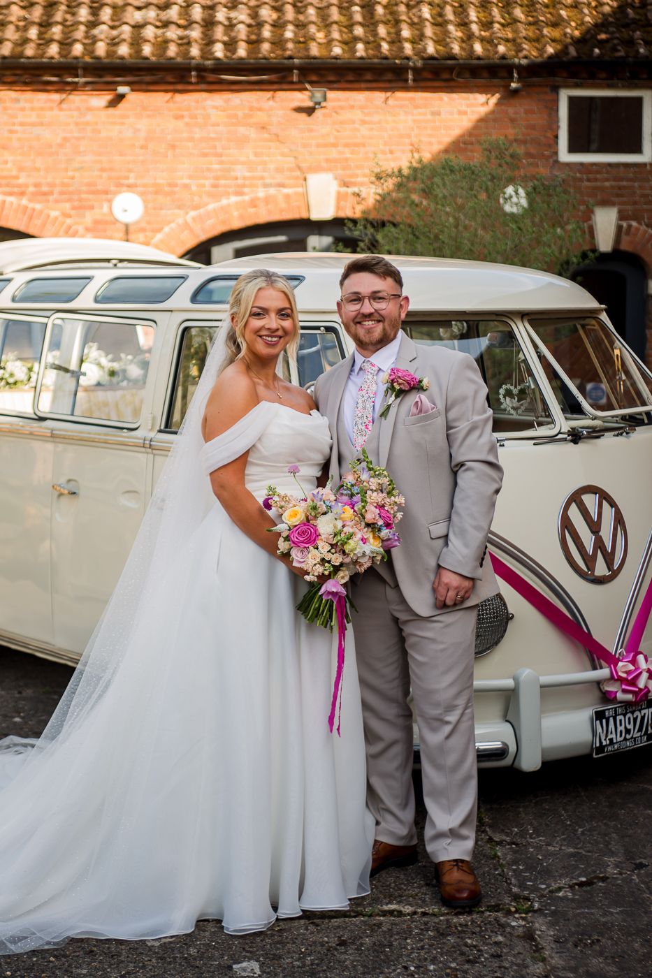 Classic white VW campervans lined up against a brick wall create a vintage wedding scene.