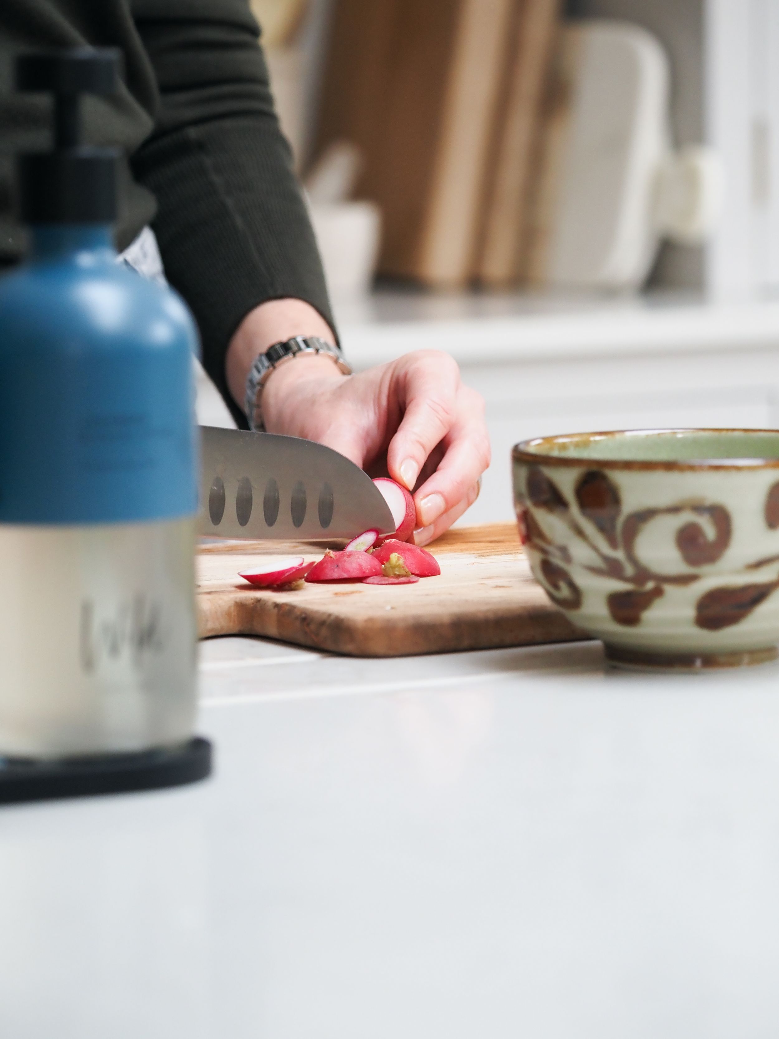 Person slicing fresh red radishes on a wooden cutting board with a chef knife in a modern kitchen.