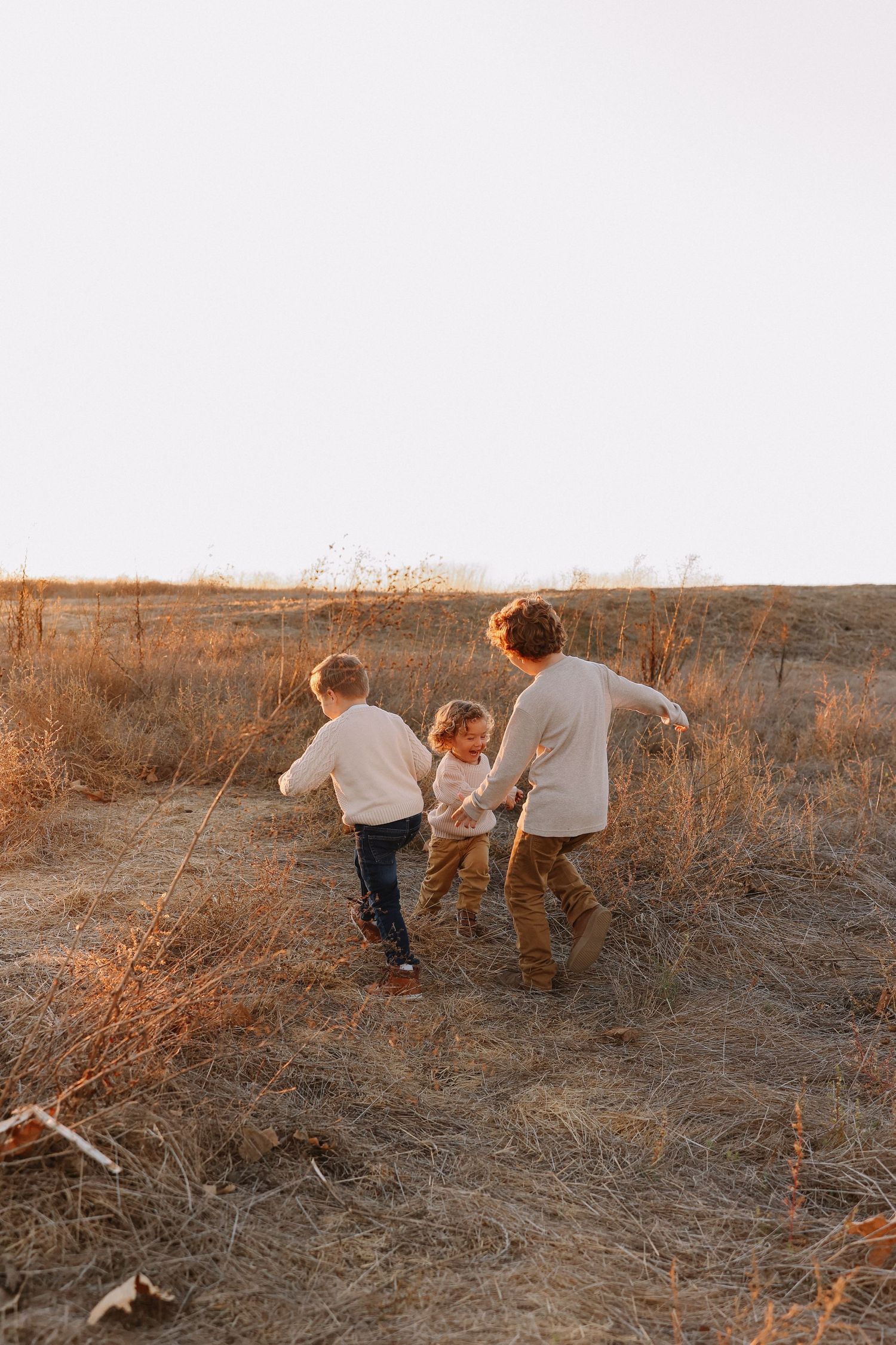 Candid Orange County family photo with kids laughing and running through tall grass
