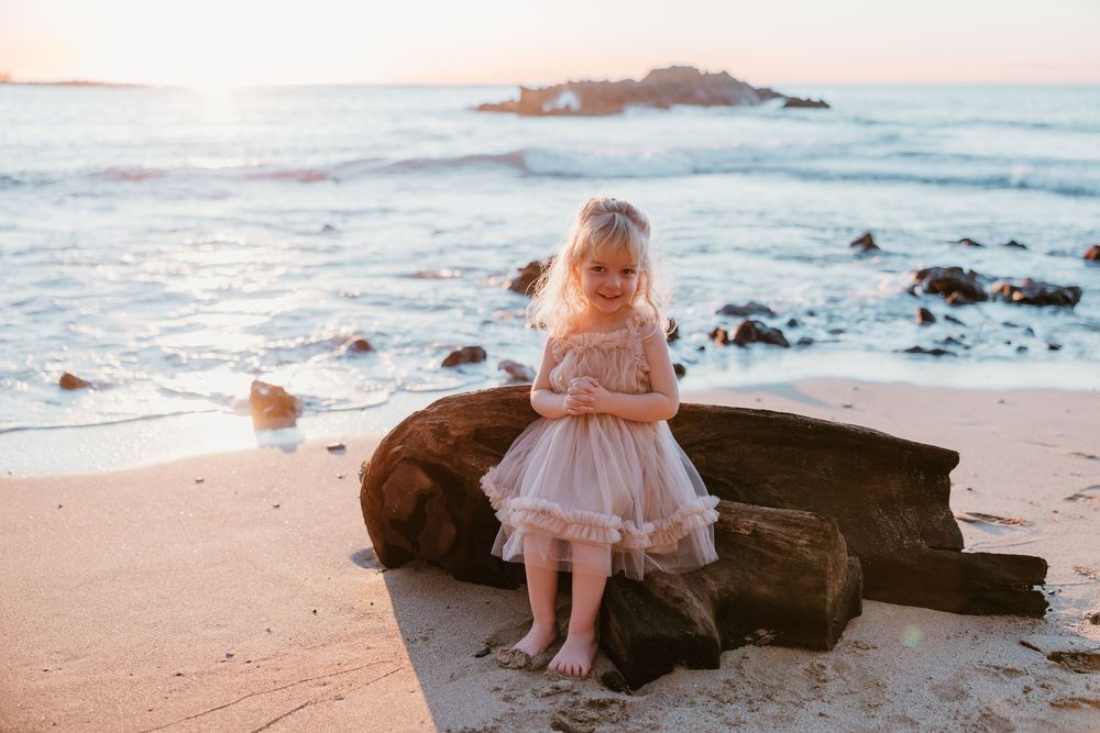 A series of beach photos at sunset showing a toddler in a pink dress exploring the rocky shoreline and sand.