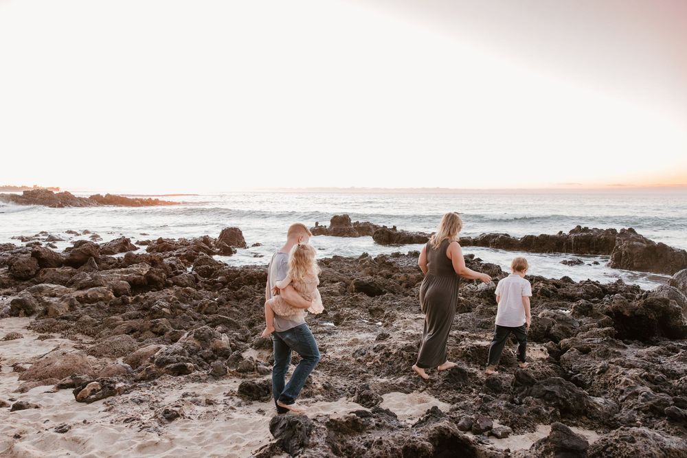 A romantic sunset photoshoot on a rocky beach with soft golden light illuminating the coastal landscape.
