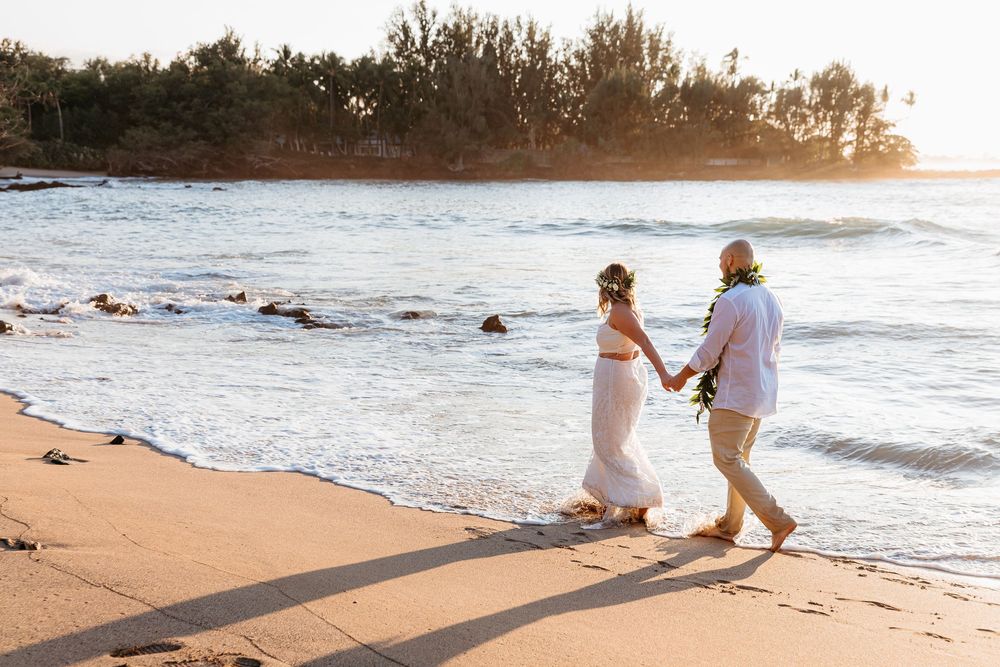 A couple walks along a scenic beach at sunset during a romantic photoshoot.