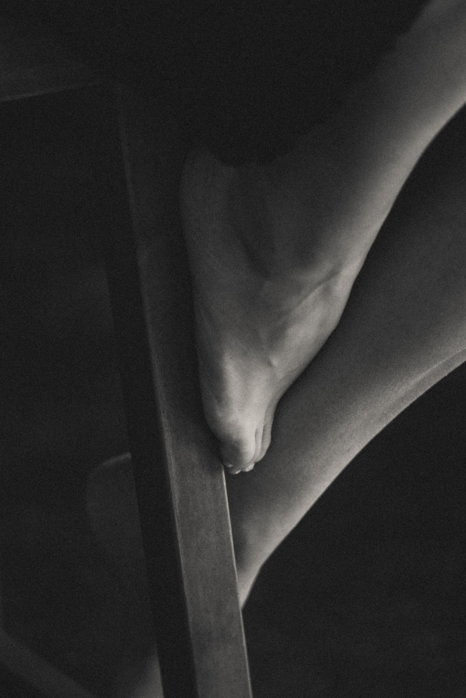 Artistic close-up of bare foot and chair in black and white, minimalist boudoir detail.