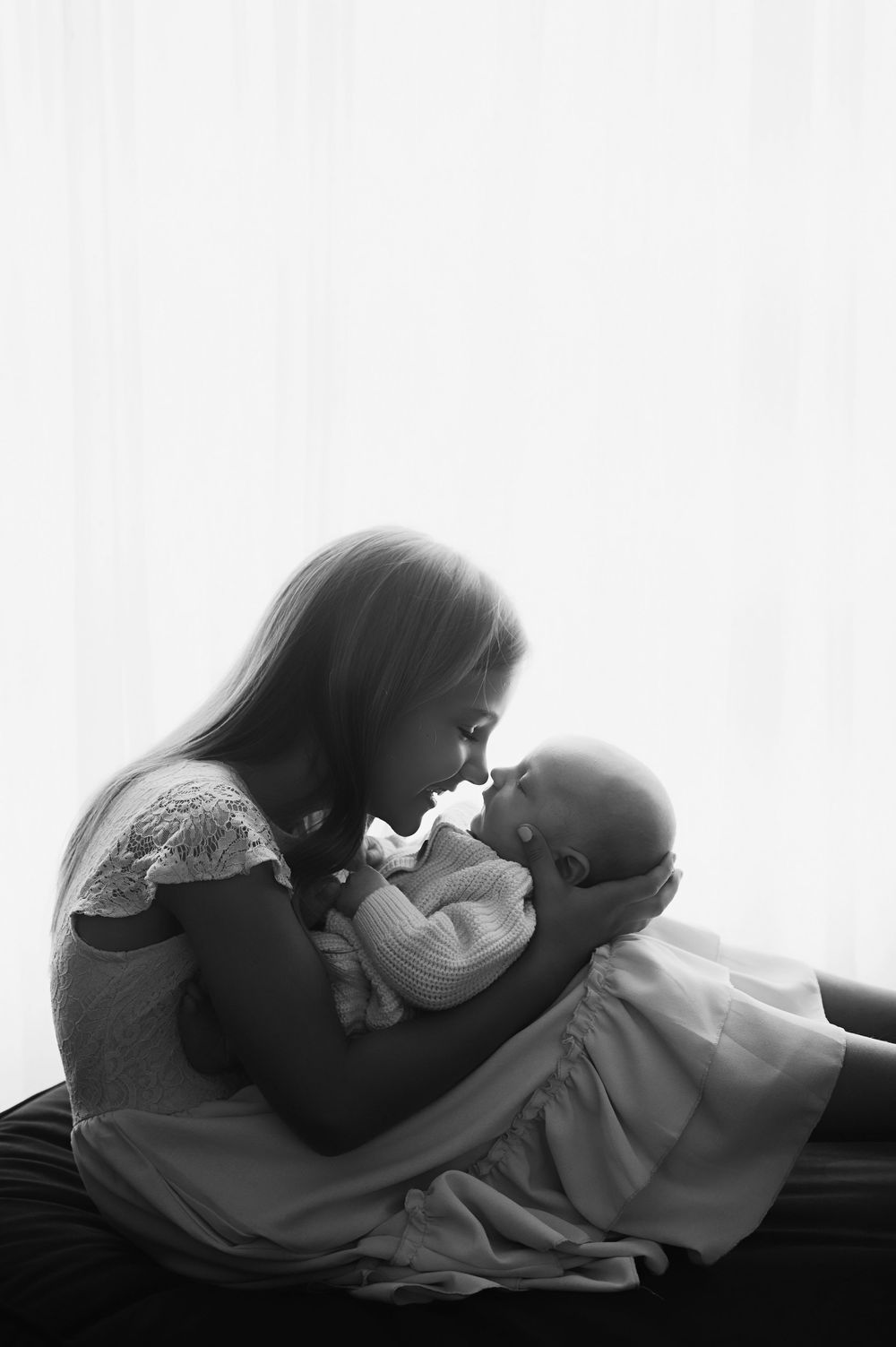 A black and white photo series showing a tender moment between sibling and infant in silhouette.