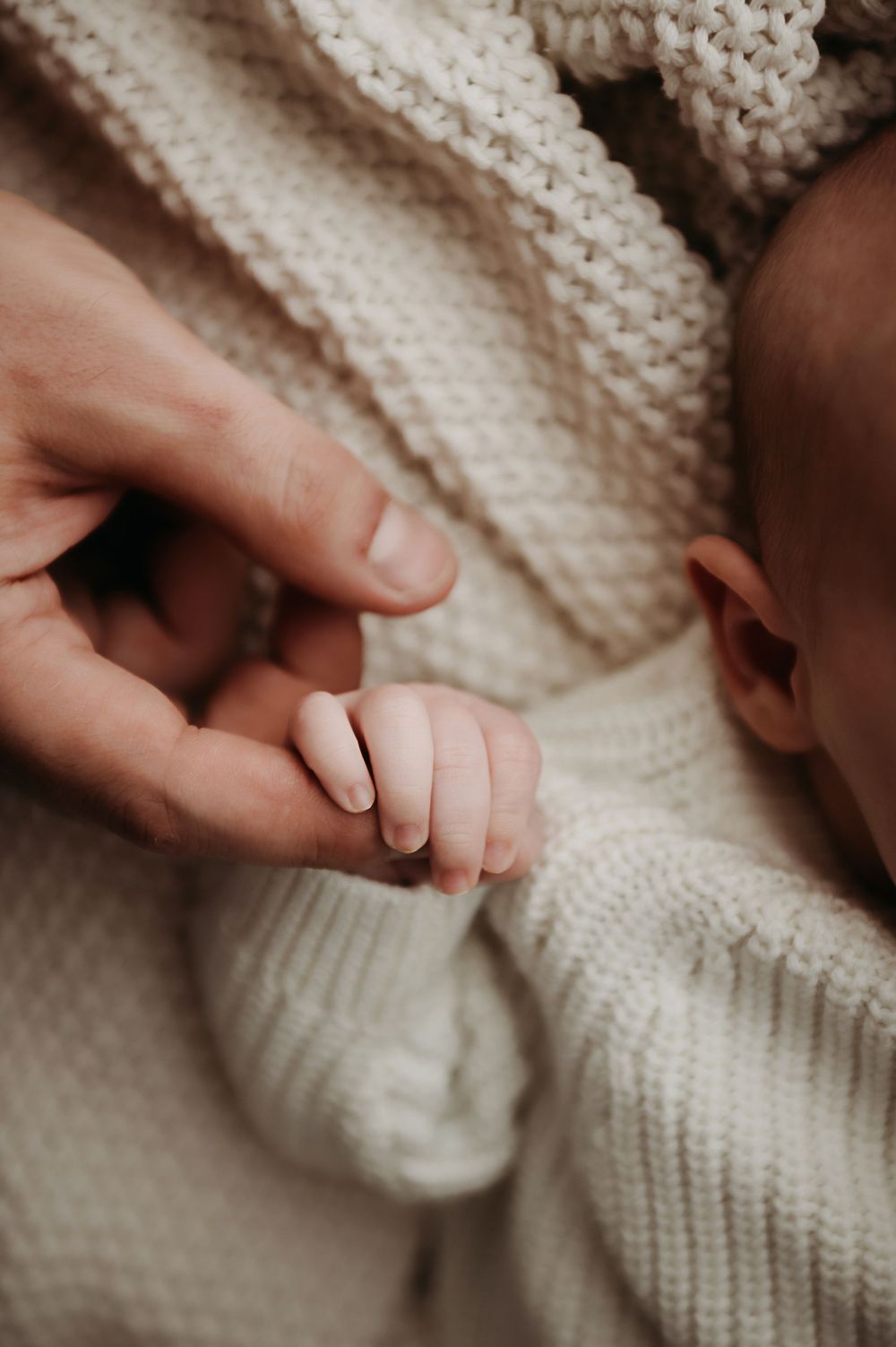 Close-up of gentle hands touching soft white knitted fabric texture in warm natural lighting.
