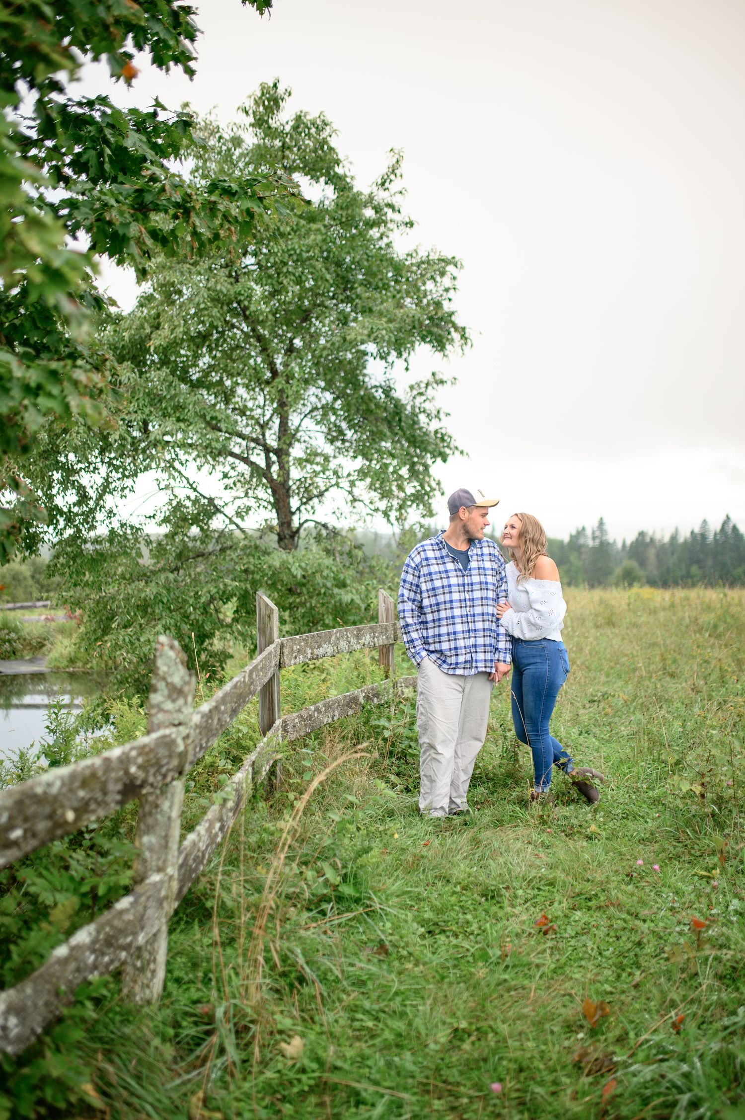 Couple embracing on grassy hillside under tree branches in romantic outdoor setting.