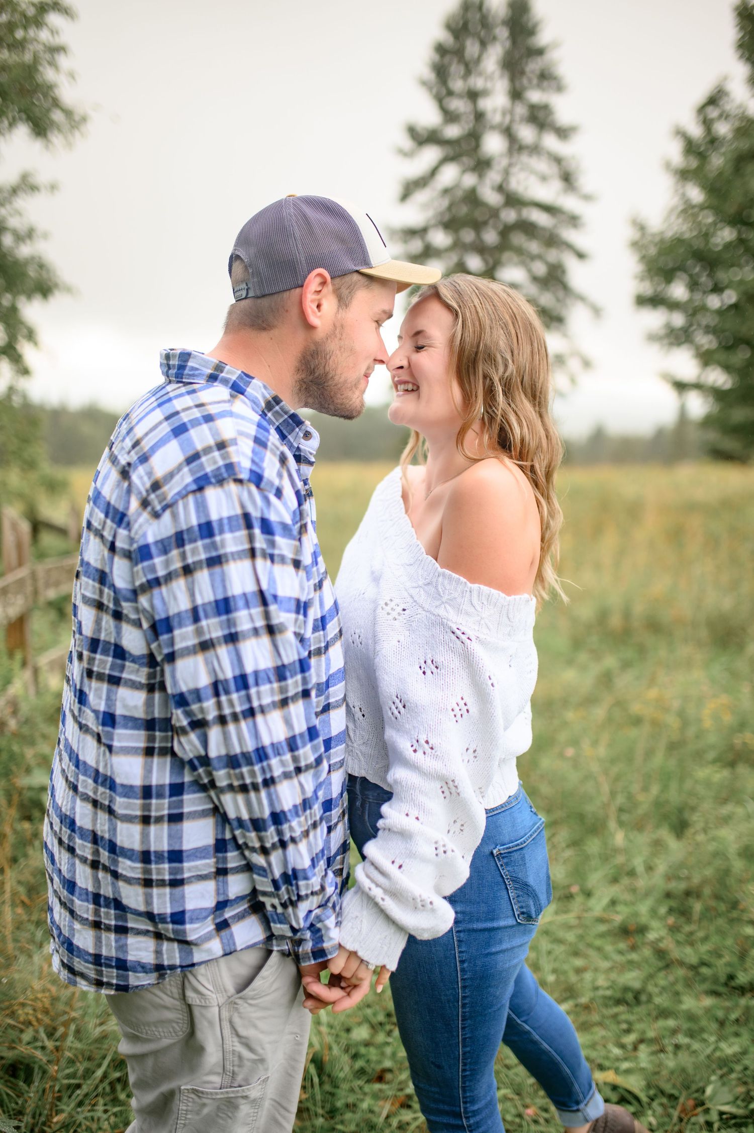 A couple shares a romantic moment in a field with evergreen trees in the background.