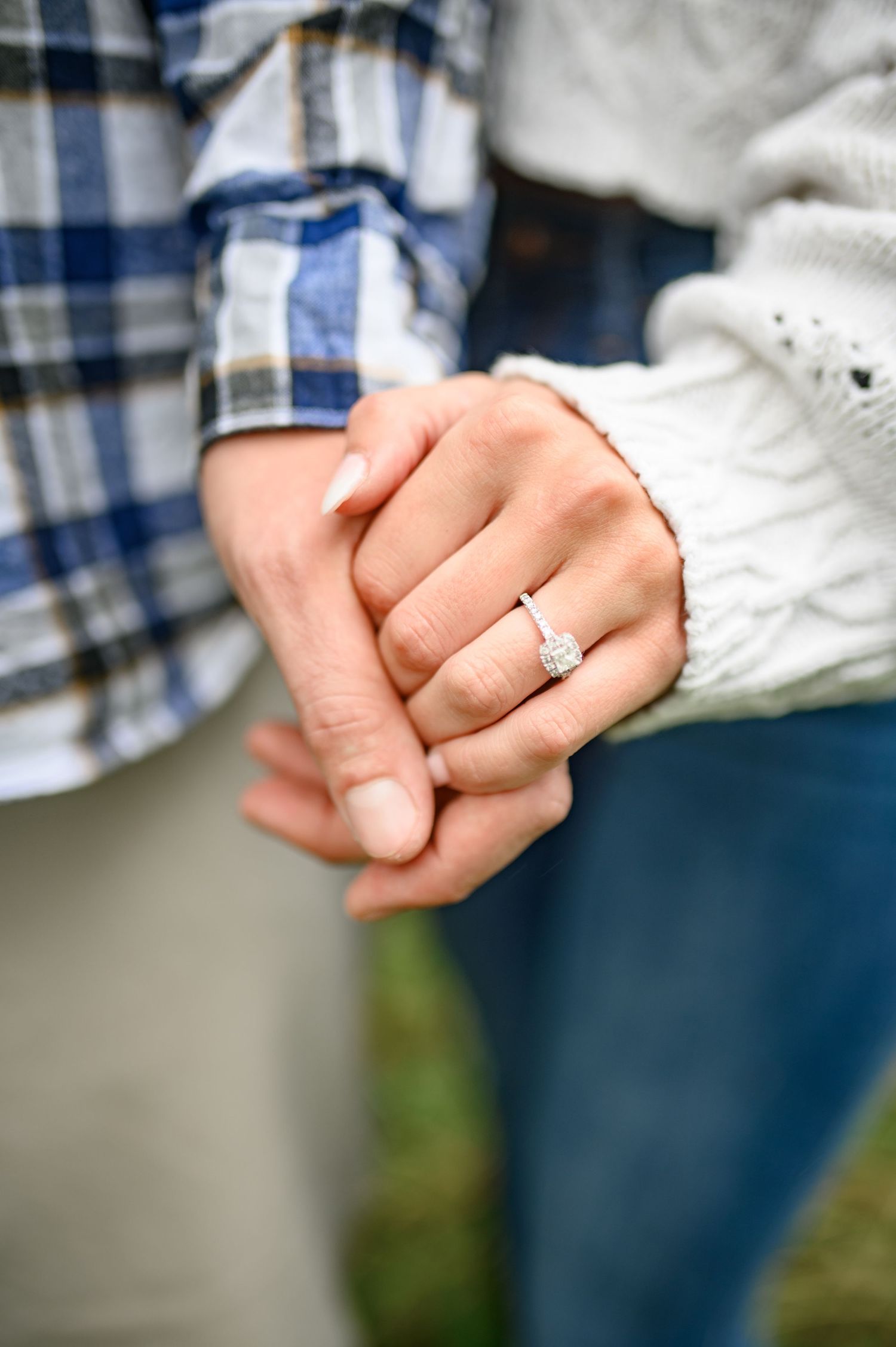 Close-up view of intertwined hands wearing wedding rings against a casual clothing background.